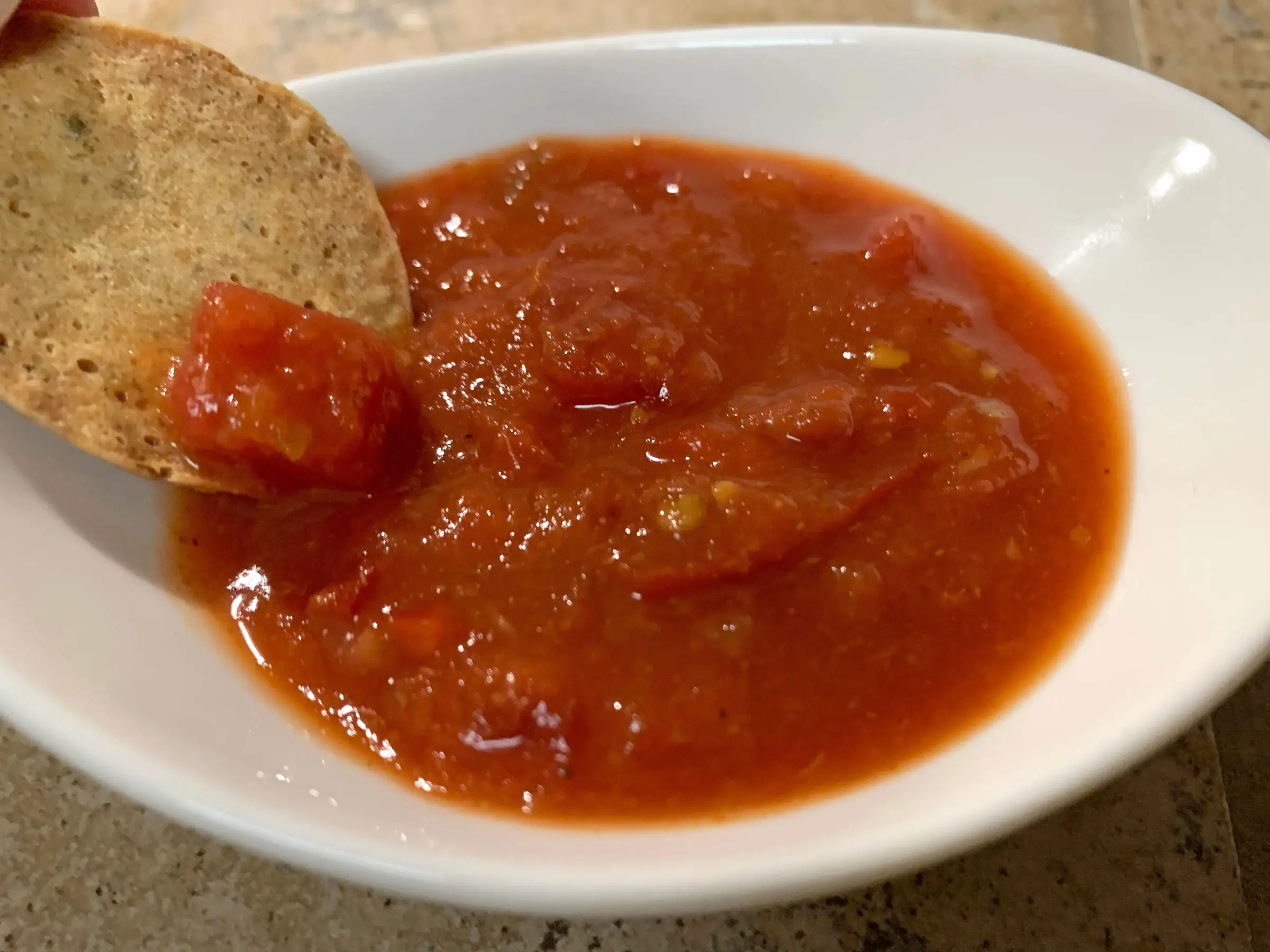 A chip being dipped in Trader Joe's Bloody Mary salsa, which is in a small white bowl.