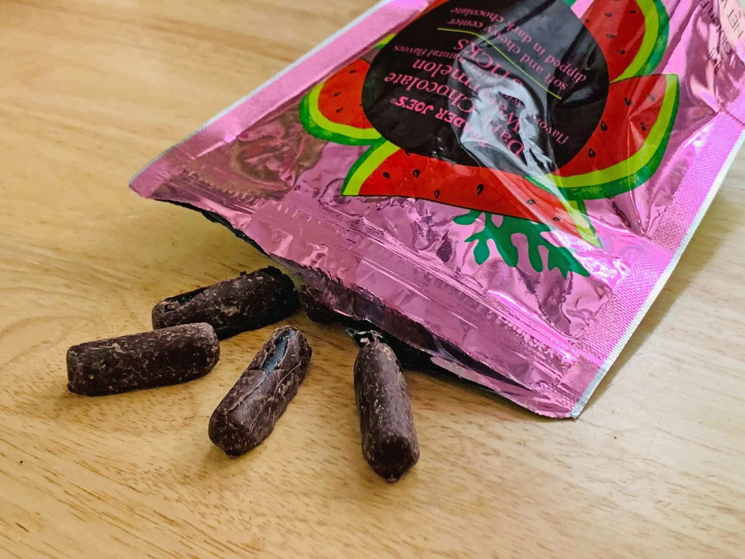 Trader Joe's chocolate watermelon sticks spilling out of the pink packaging on a light-wood table.