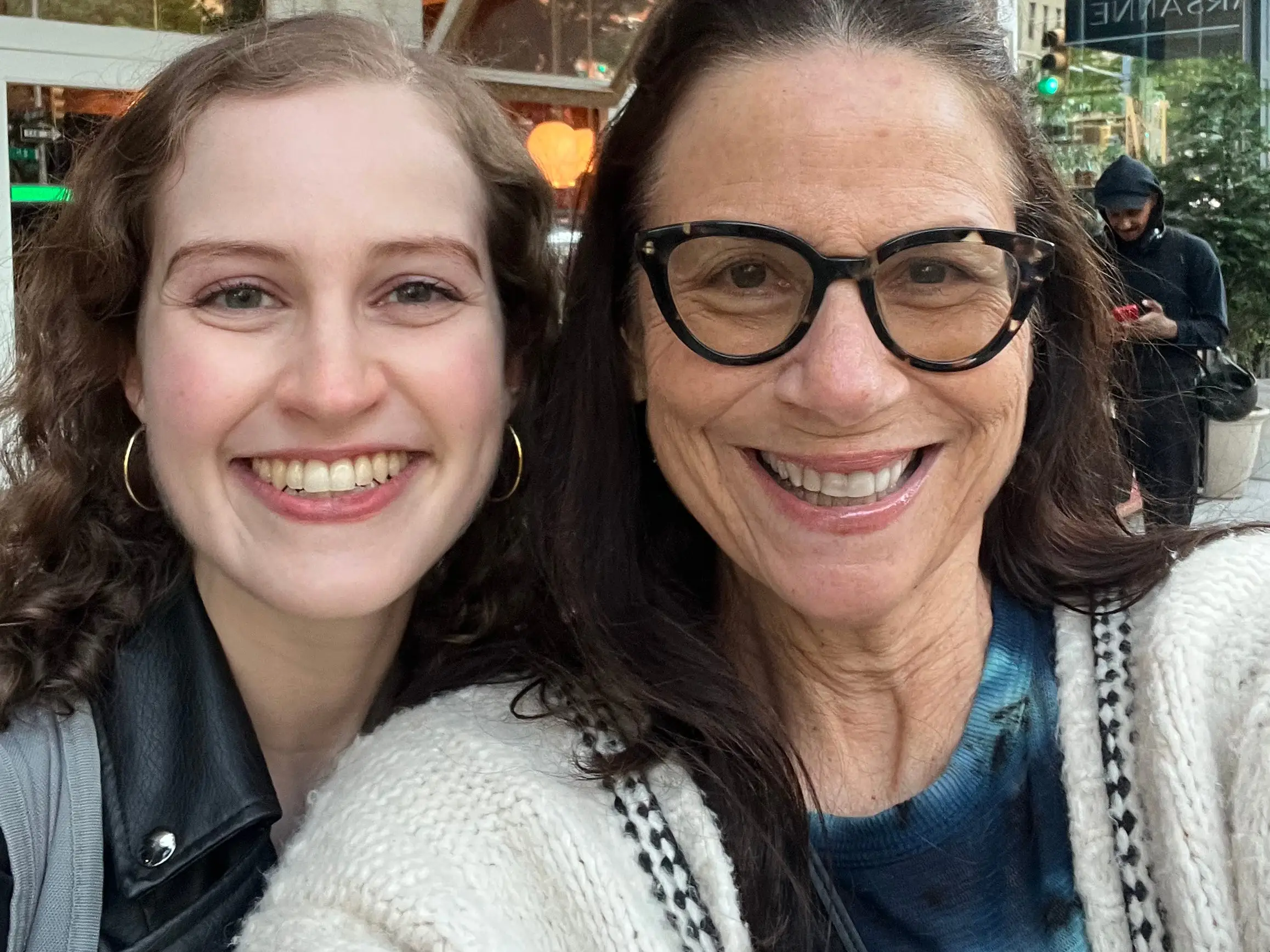 Two smiling people pose for a selfie outside a Fellini storefront with a burgundy awning.