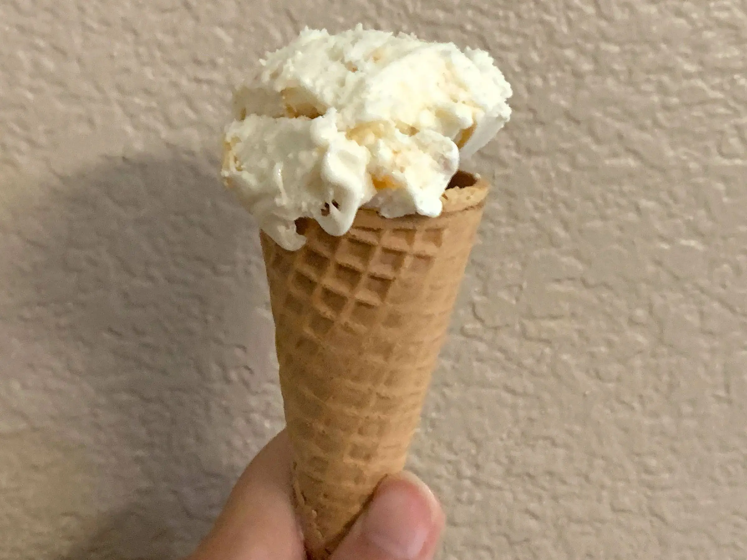 A hand holding an ice-cream cone with white ice cream.