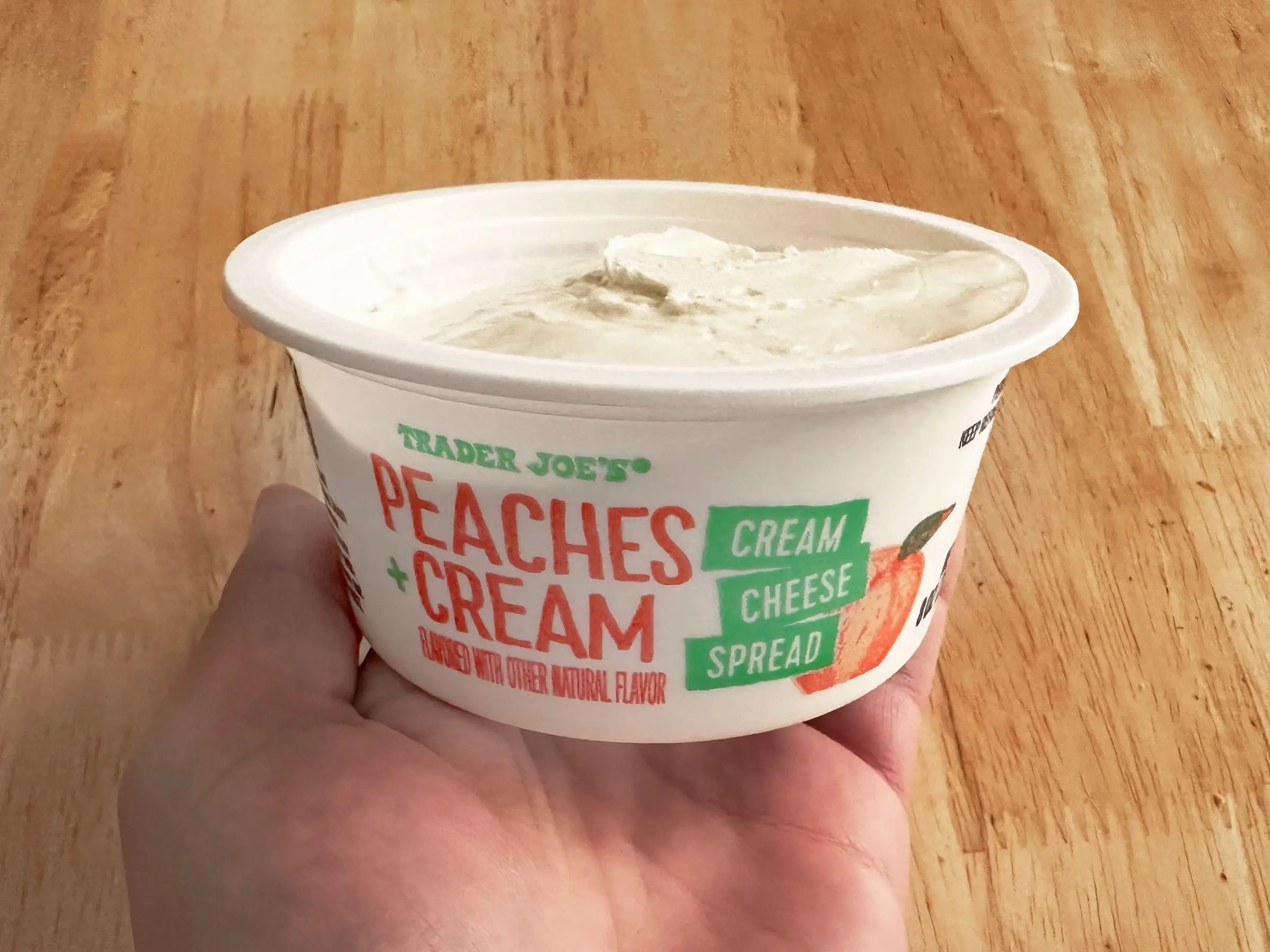 A hand holding a container of Trader Joe's peaches-and-cream spread.