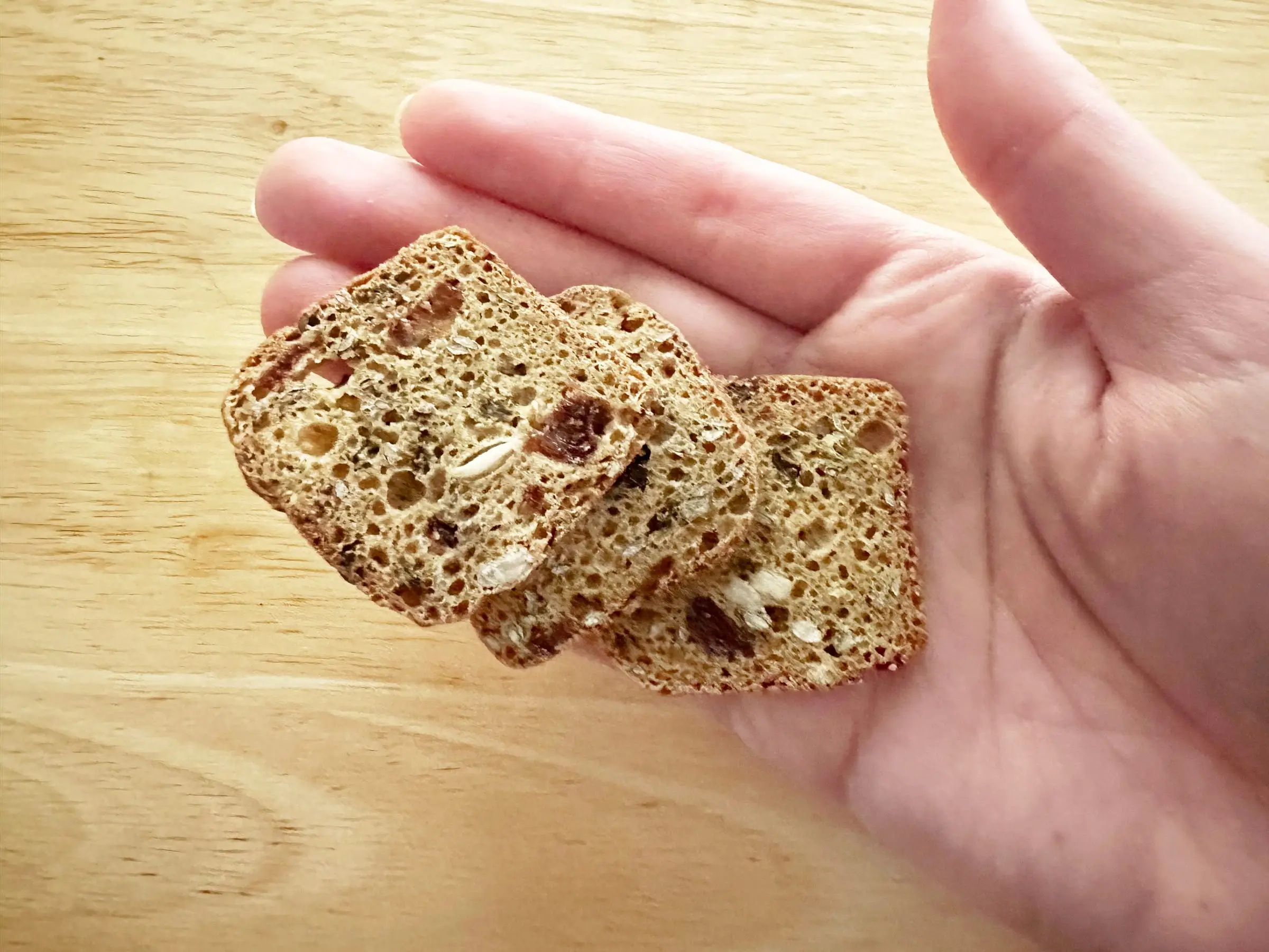 A hand holds three small crackers that look like small pieces of bread, with dried pieces of strawberries in them.