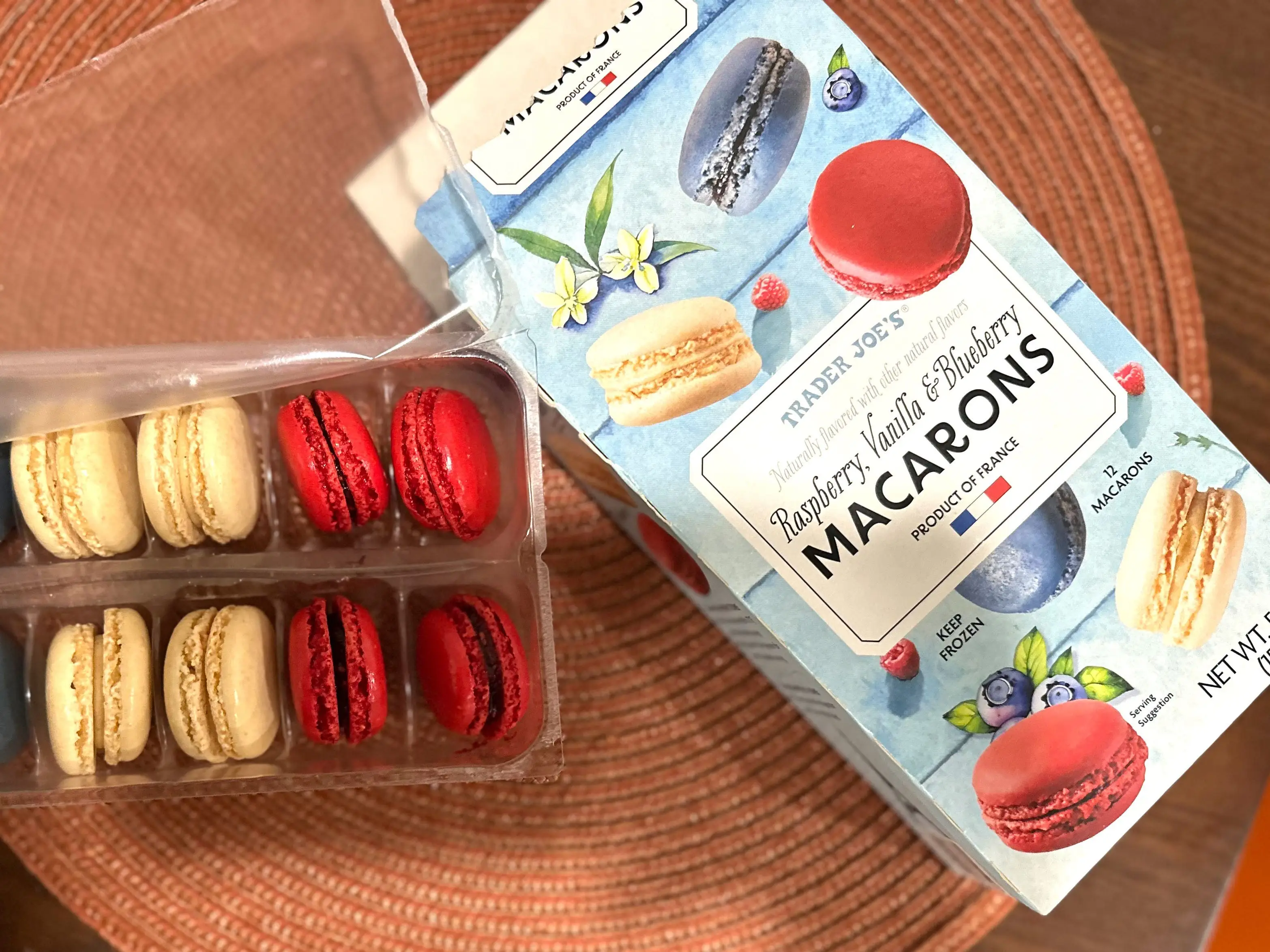 A box of Trader Joe's raspberry, vanilla, and blueberry macarons next to an open container of the product.