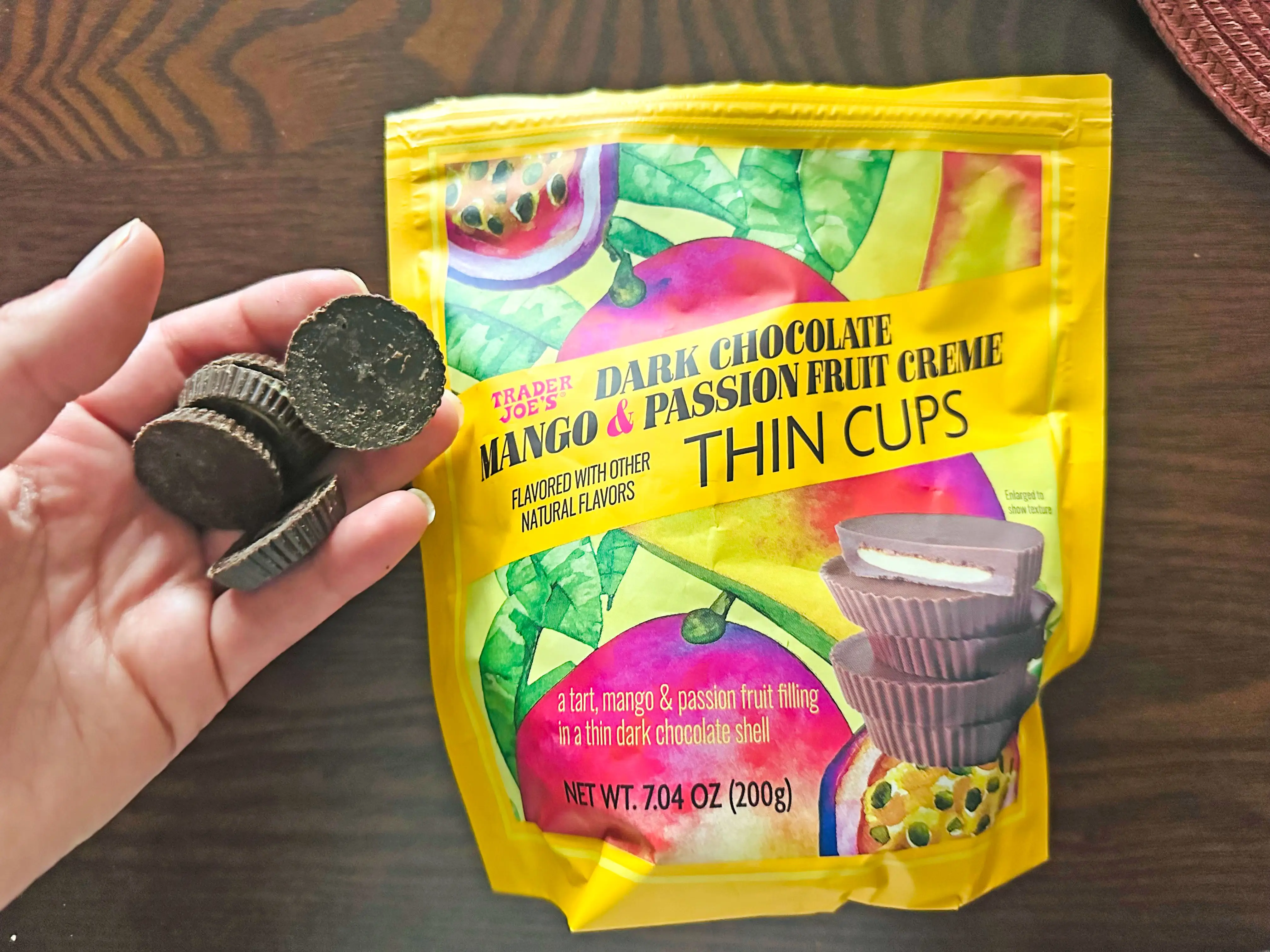 A hand holding several dark-chocolate mango-and-passionfruit creme cups next to the bag the product comes in.