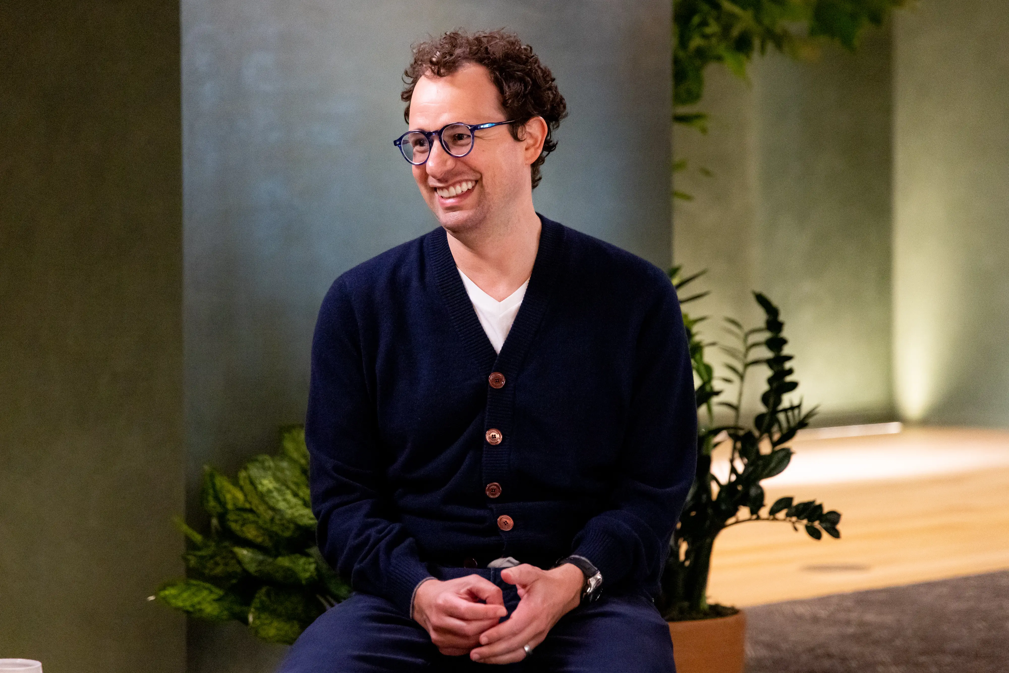 Anthropic CEO Dario Amodei is smiling while sitting in a chair.