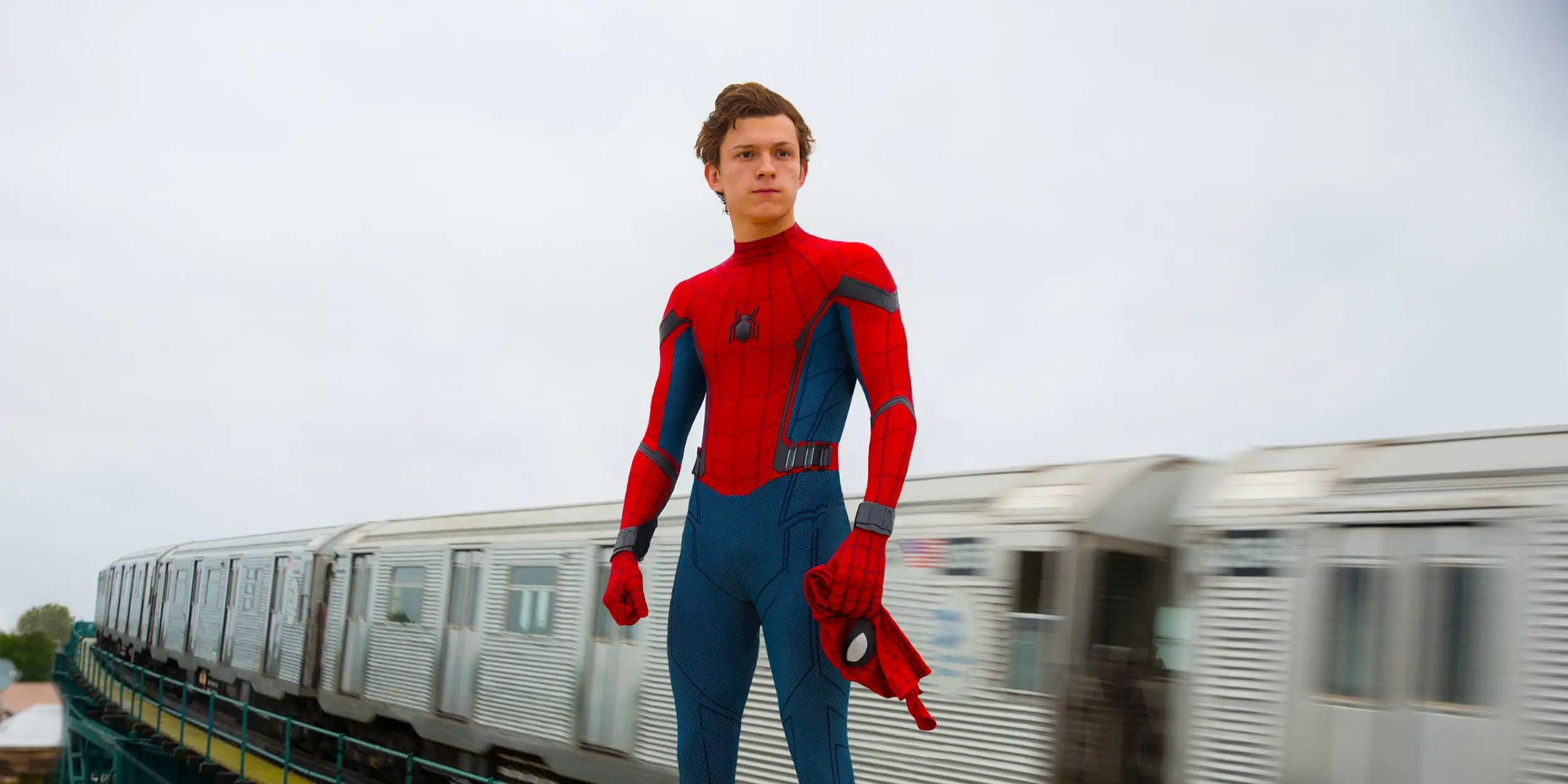 Tom Holland in Spider-man suit stand by a moving subway train