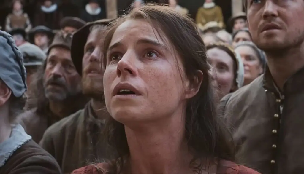 Jessie Buckley looking shocked in a crowd in Hamnet movie