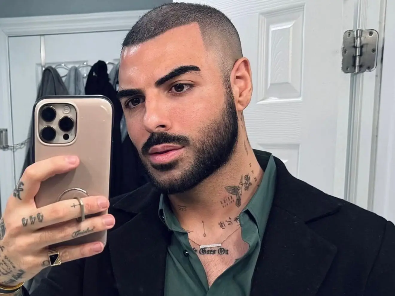 A man wearing a black jacket and a green shirt is taking a selfie in the mirror.