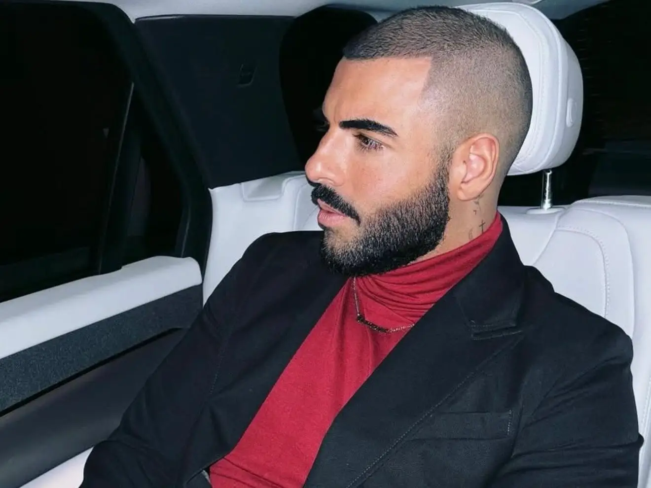 A man wearing a black jacket and red jersey looking out of a car window.