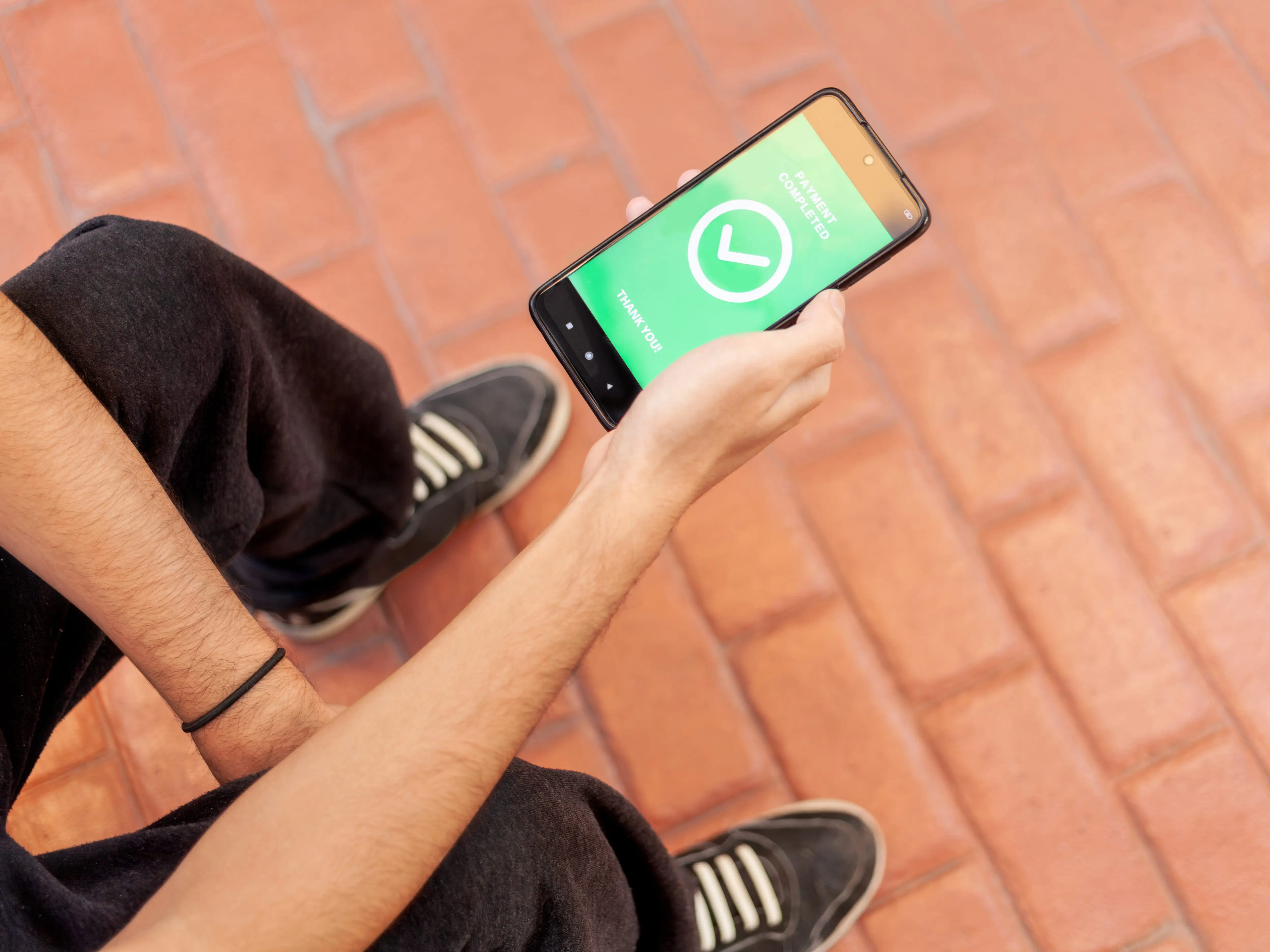 A teenager holding his phone, which is processing a digital payment.