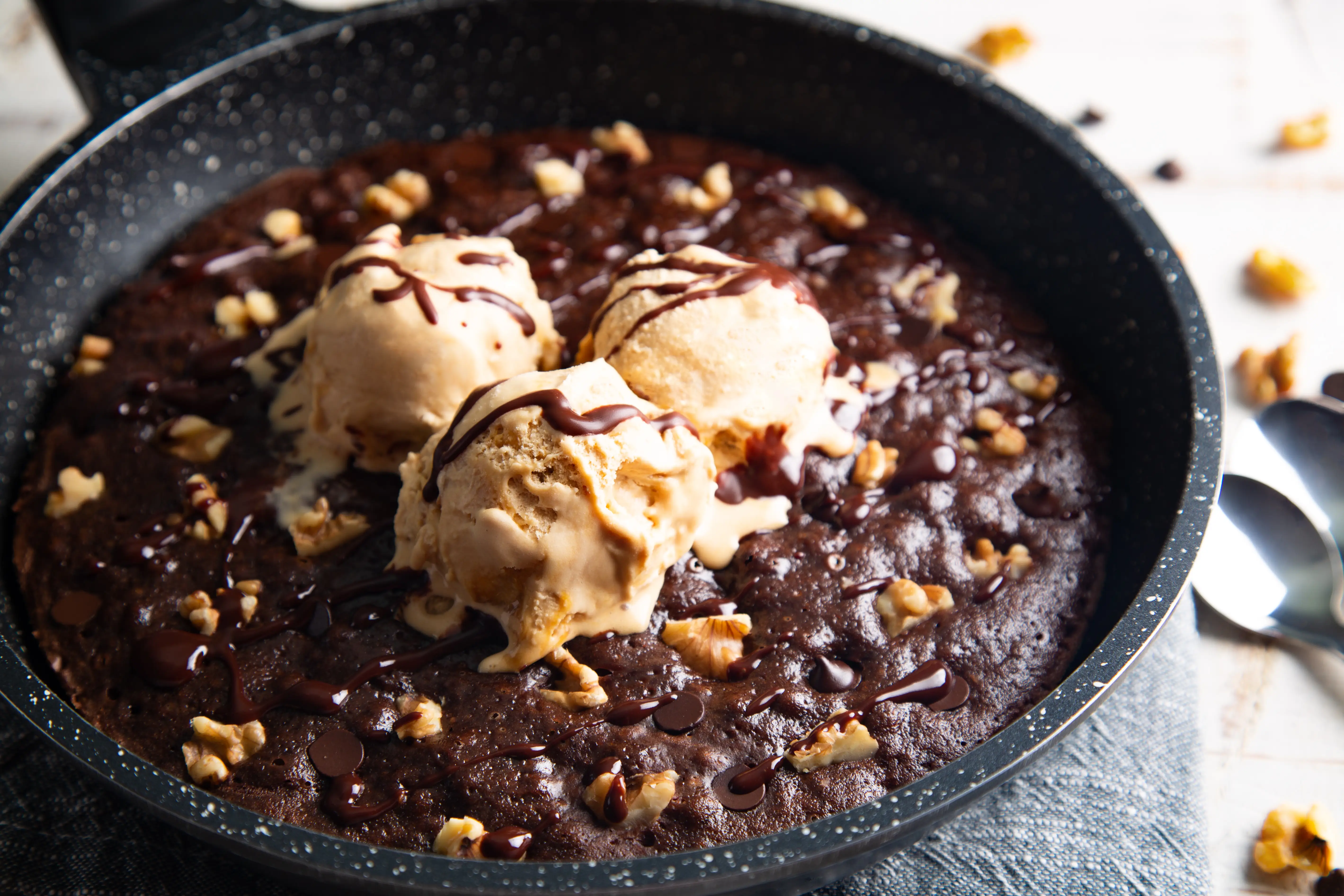Brownie in a skillet topped with nuts, ice cream