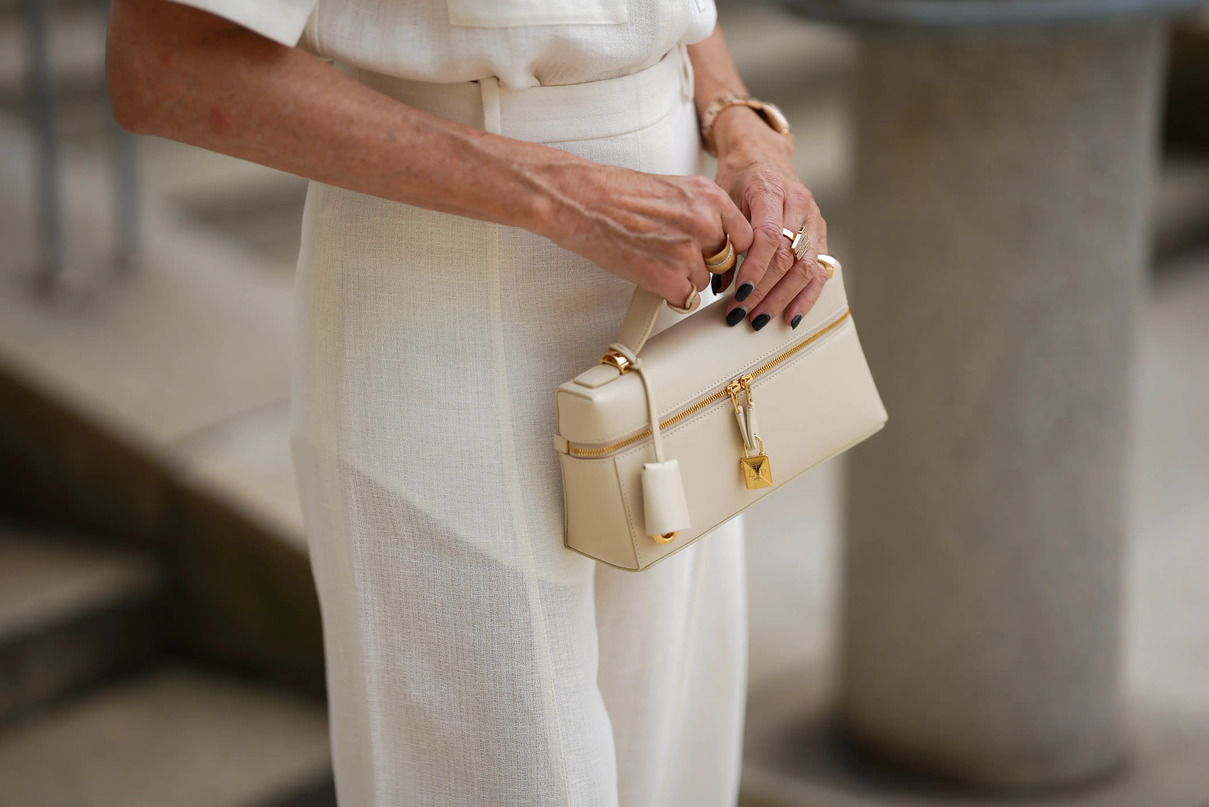 Annete Weber is seen wearing a white blouse, white baggy trousers with high waistband out of linen both from Loro Piana Summer collection; a beige mini Loro Piana leather handbag with golden buckle.