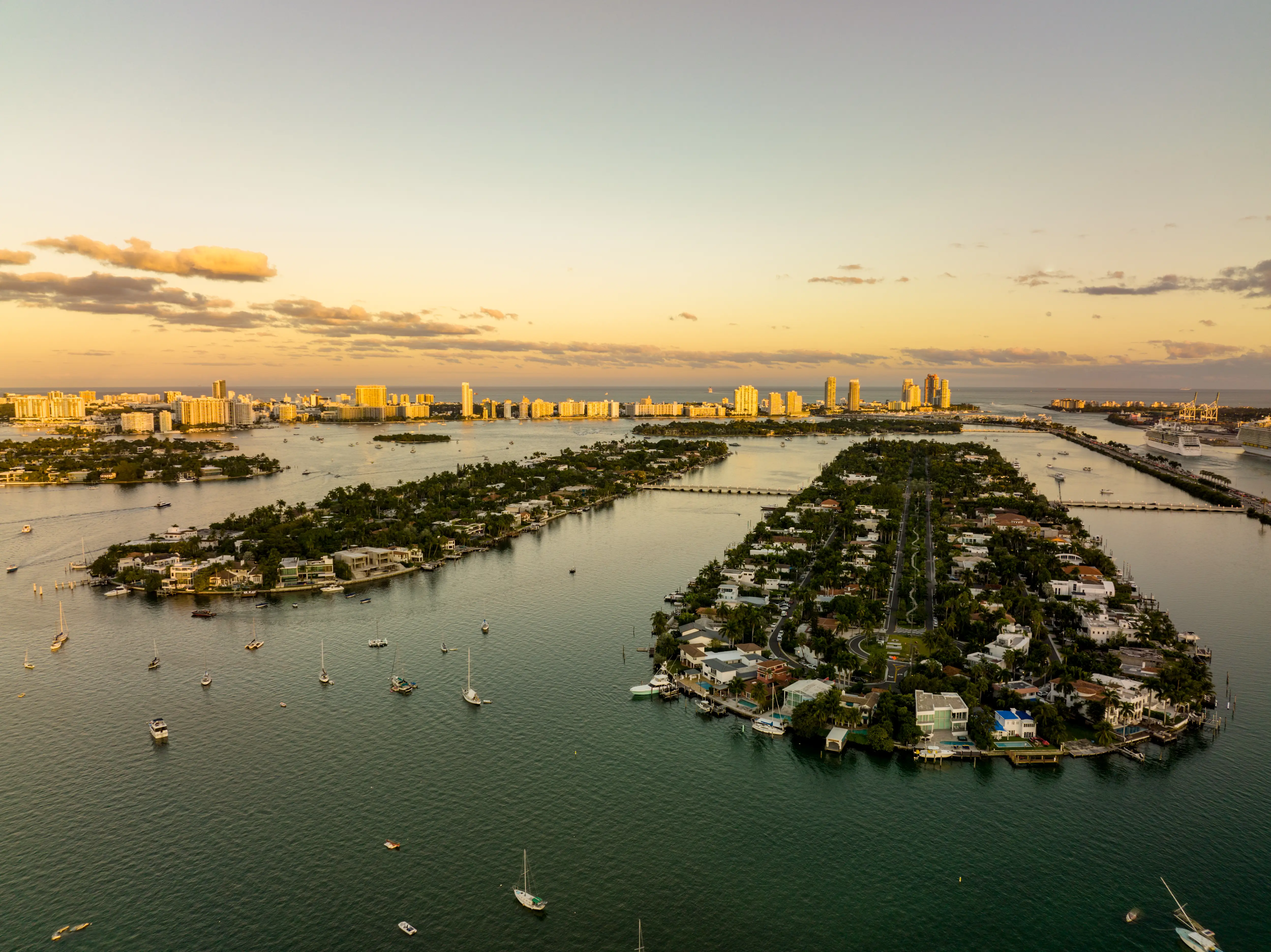 Aerial view of Biscayne Bay islands, boats, and Miami Beach skyline at sunset.