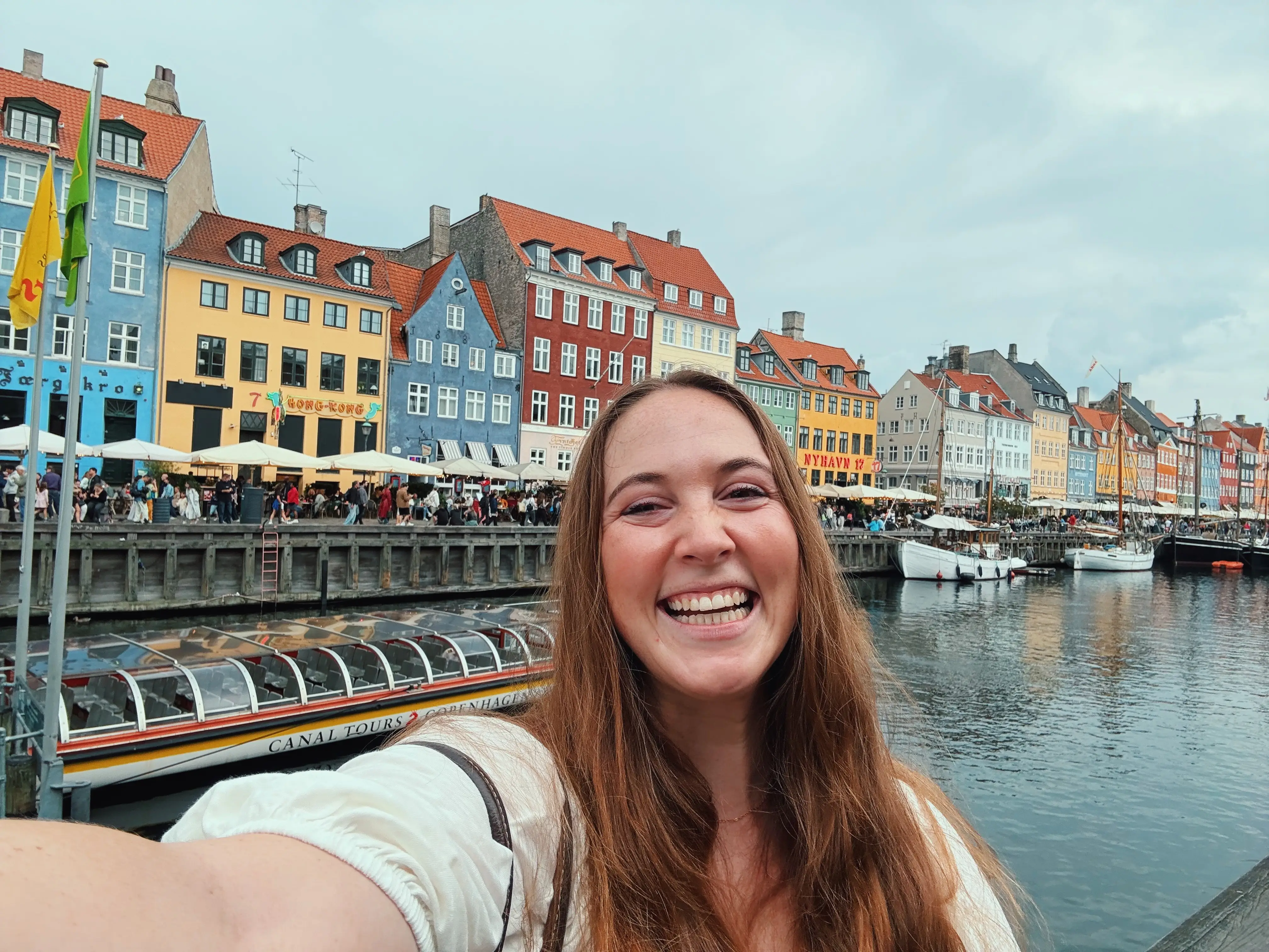 Author Allie Hubers smiling in front of boat, colorful buildings in Copenhagen