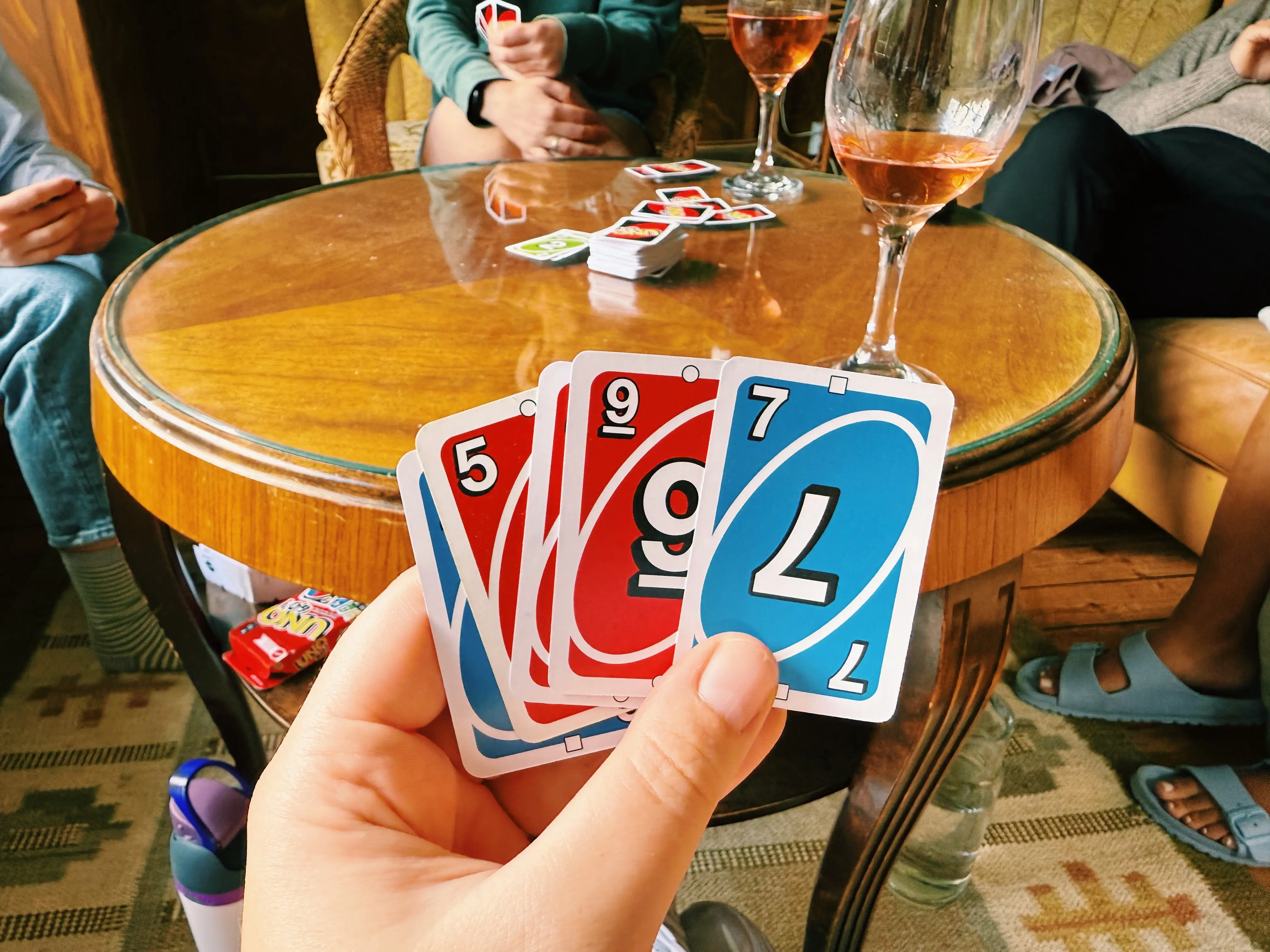 Hand holding uno cards in front of table with wine glass