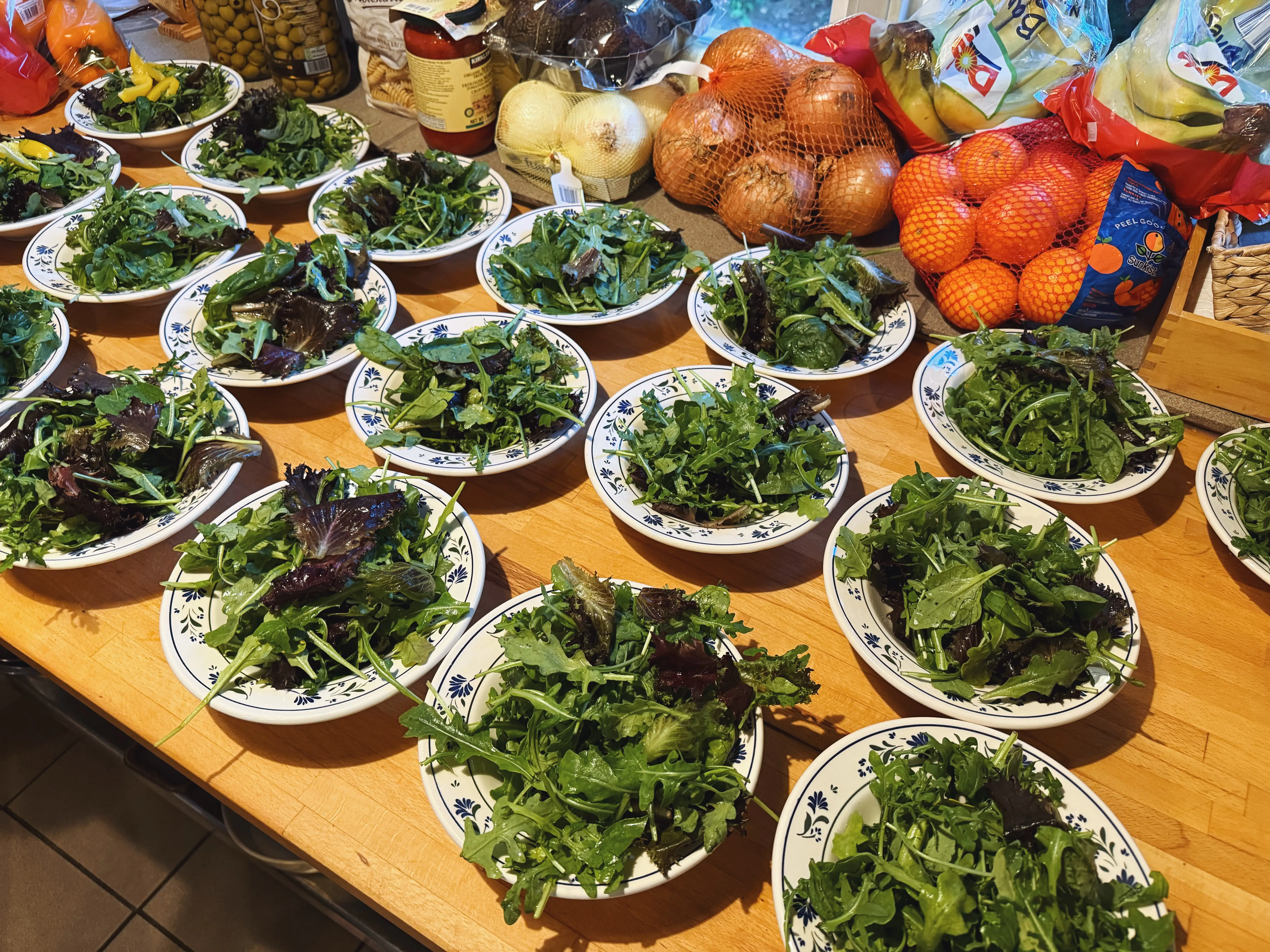 Table with several bowls with mixed greens inside and onions, oranges in background