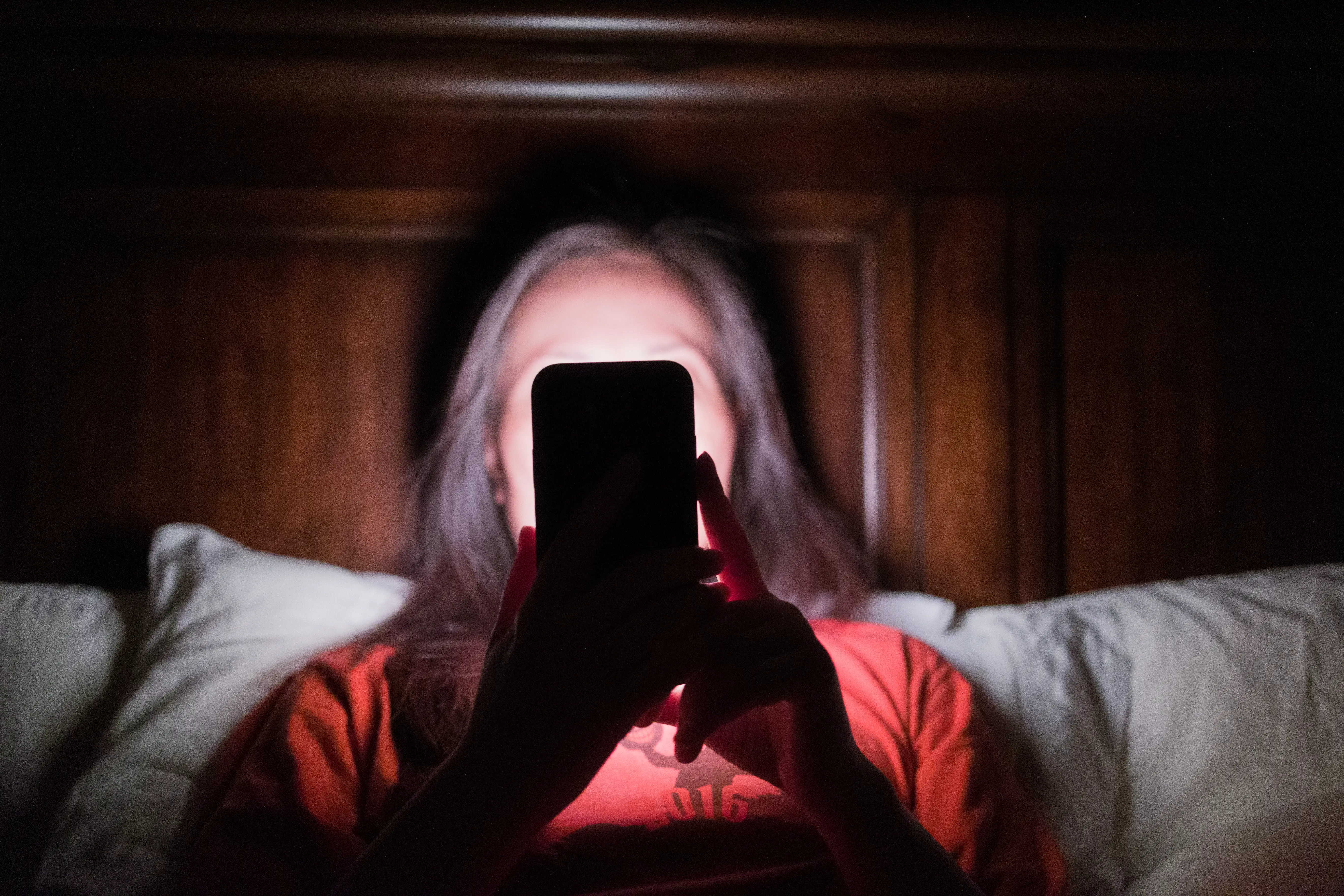 Woman's face obscured by phone in her hands in dark room