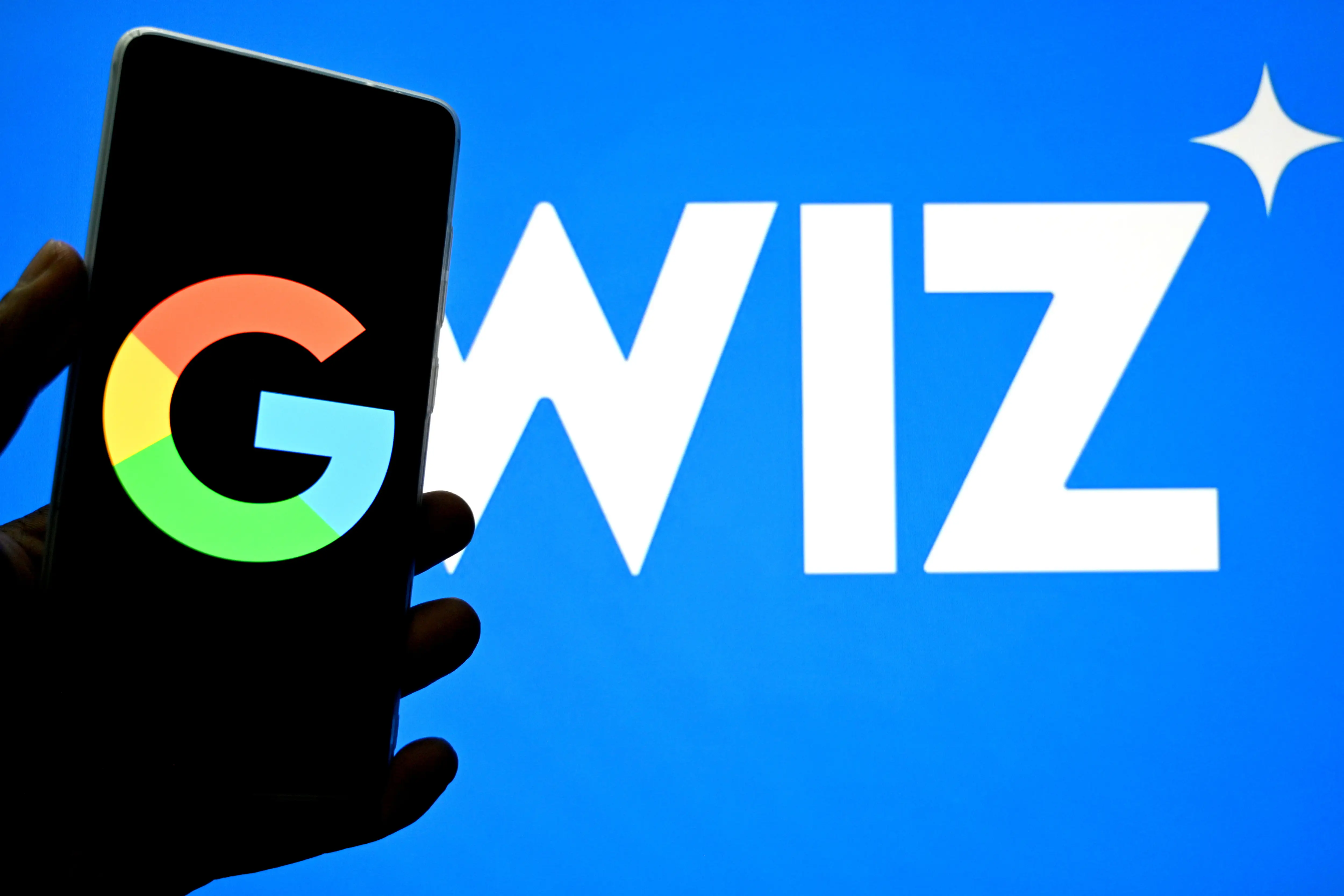 A phone with the Google logo is held over a screen that says Wiz