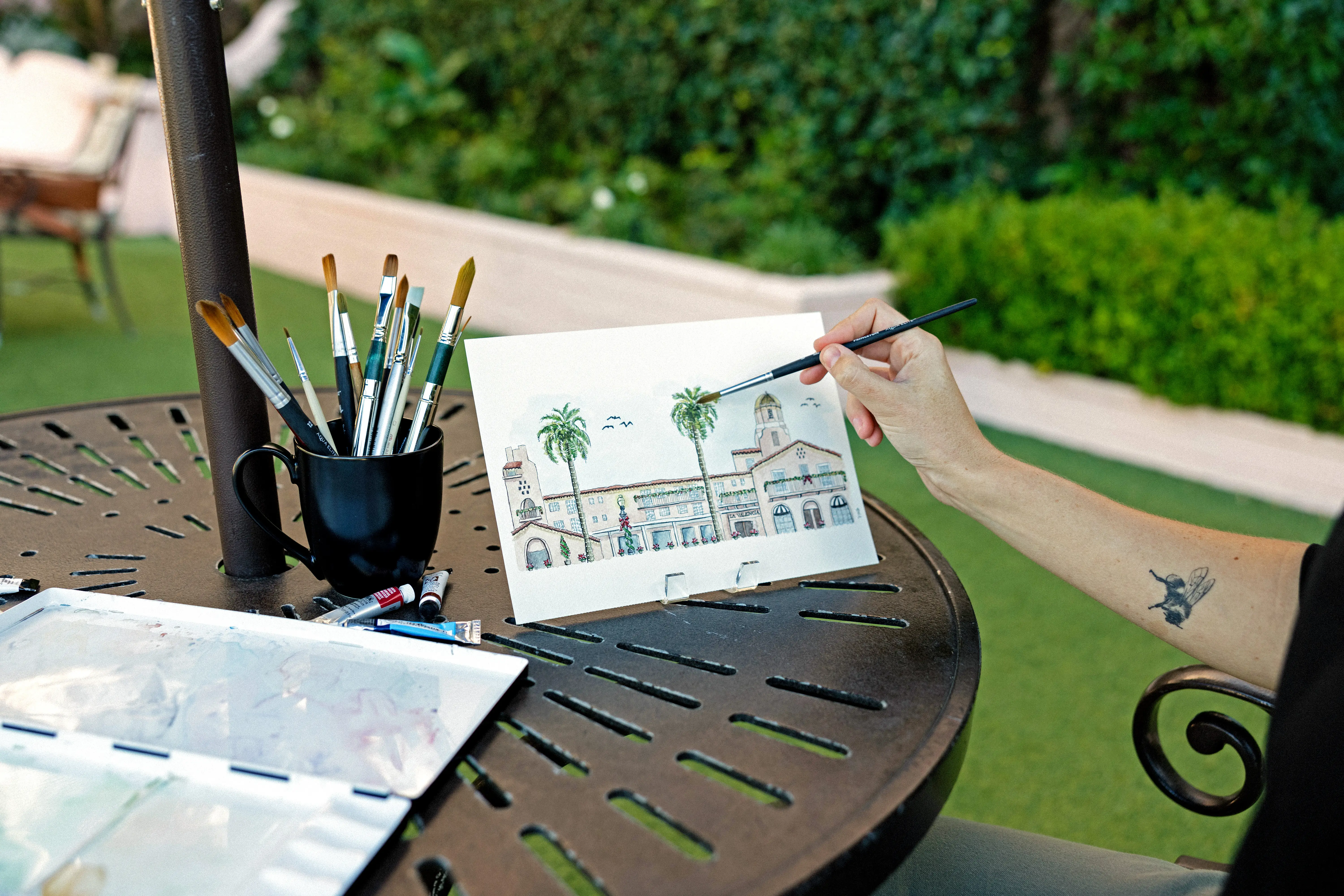 A woman painting palm trees and a tatoo on their arm.