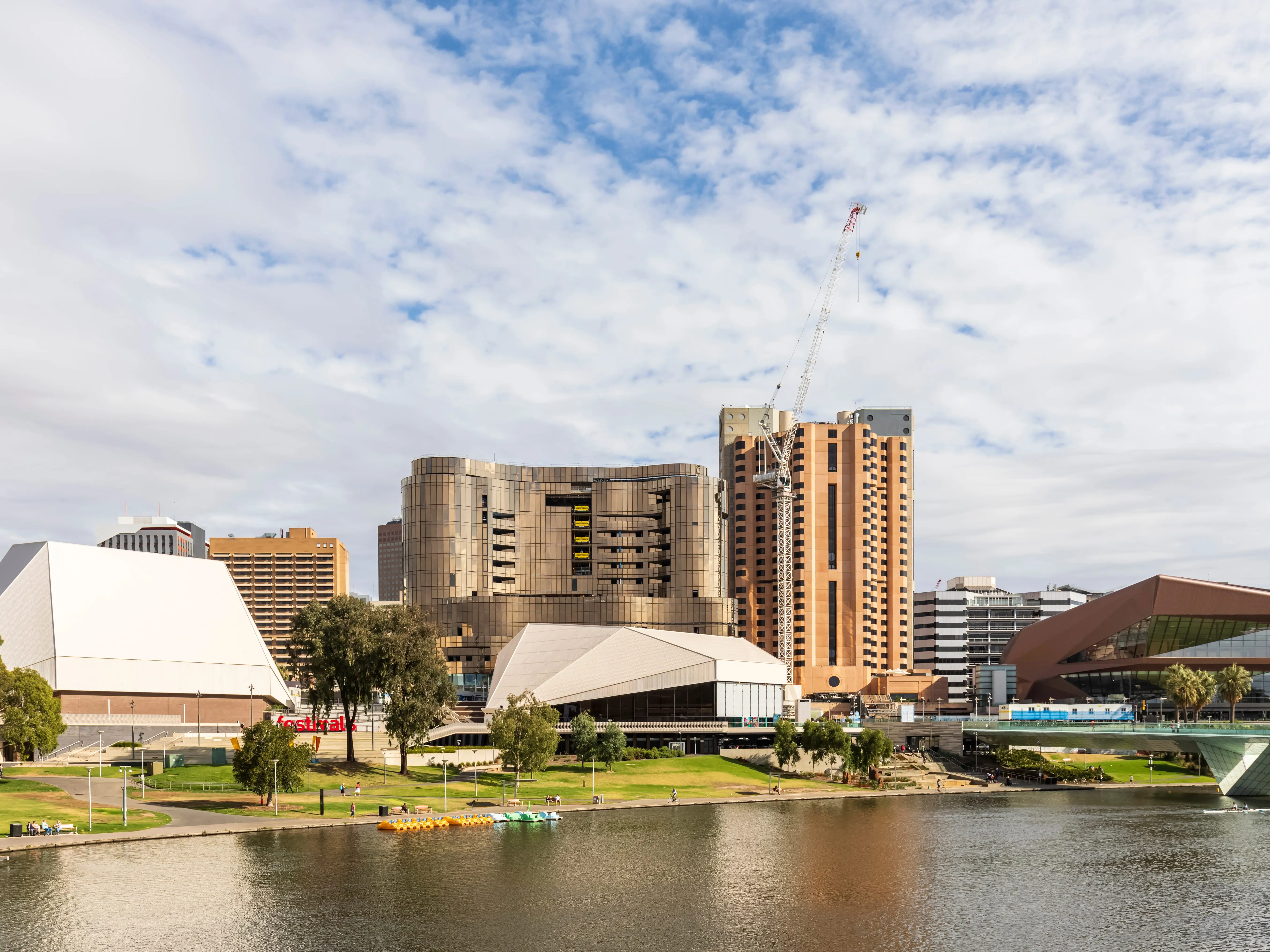 Adelaide riverfront skyline with buildings and a construction crane. A body of water is in the foreground.