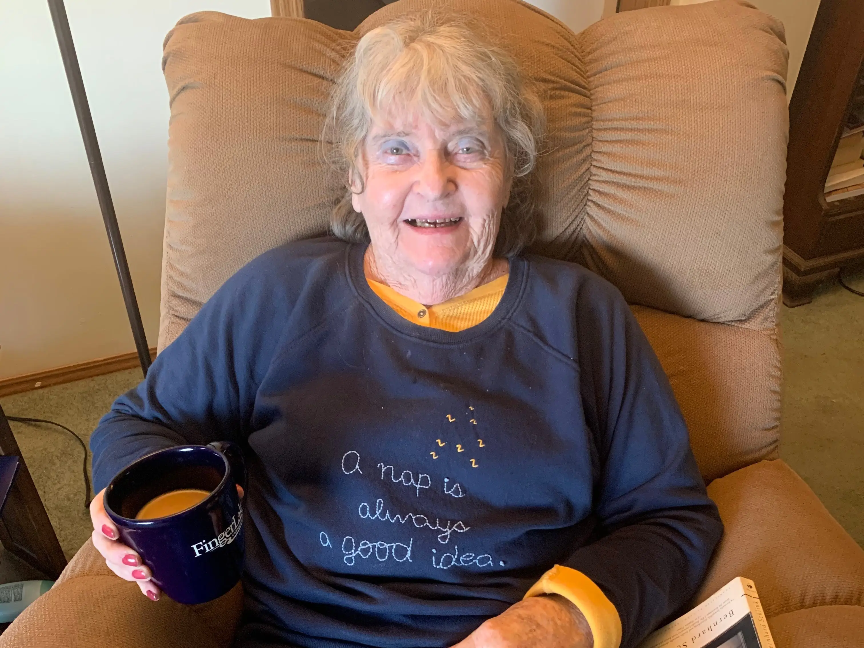 Alison's grandma sits in a recliner, holding a cup of coffee.