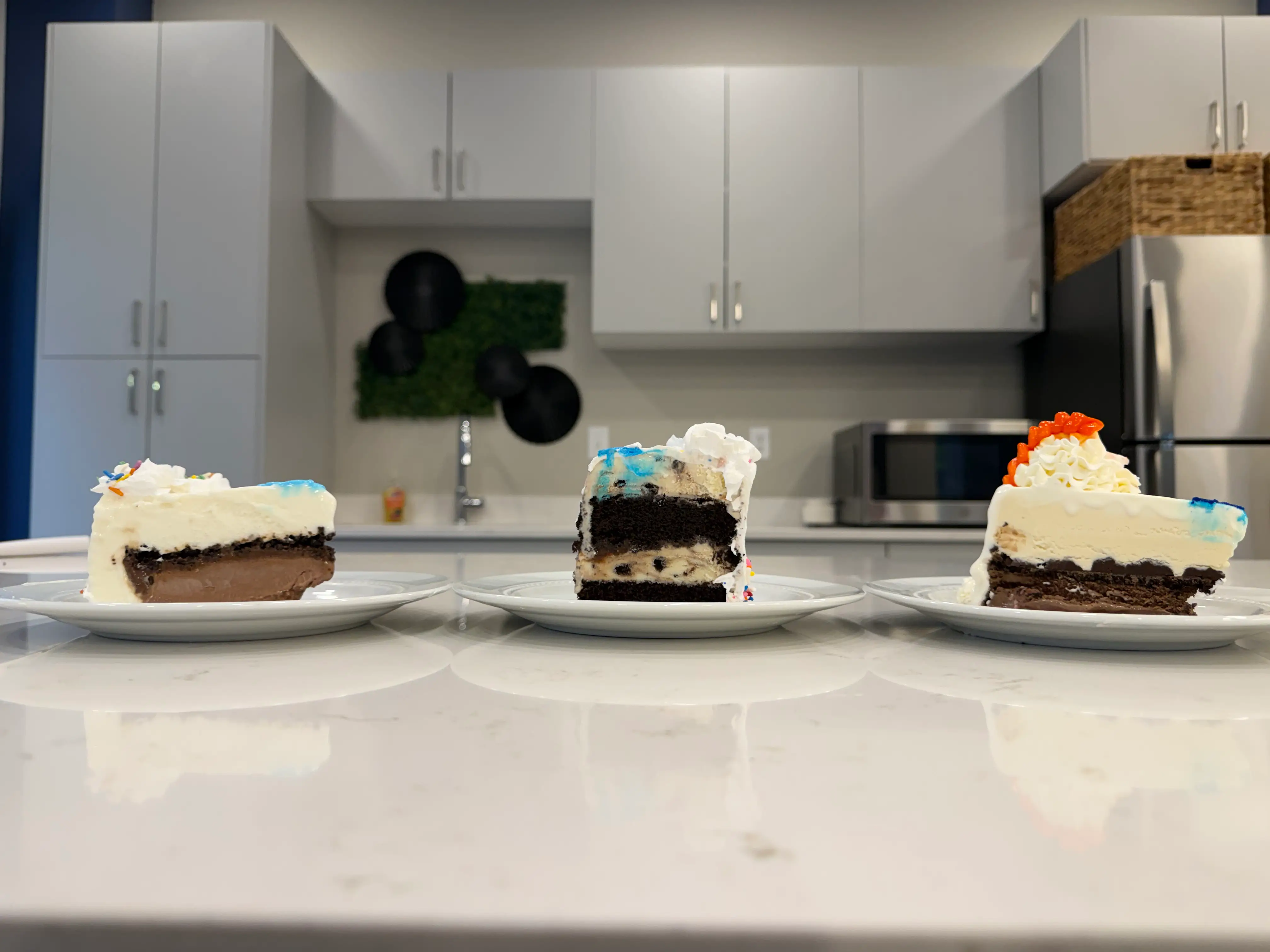 Slices of white ice cream cakes from Dairy Queen, Cold Stone Creamer, and Baskin Robbins on marble counter