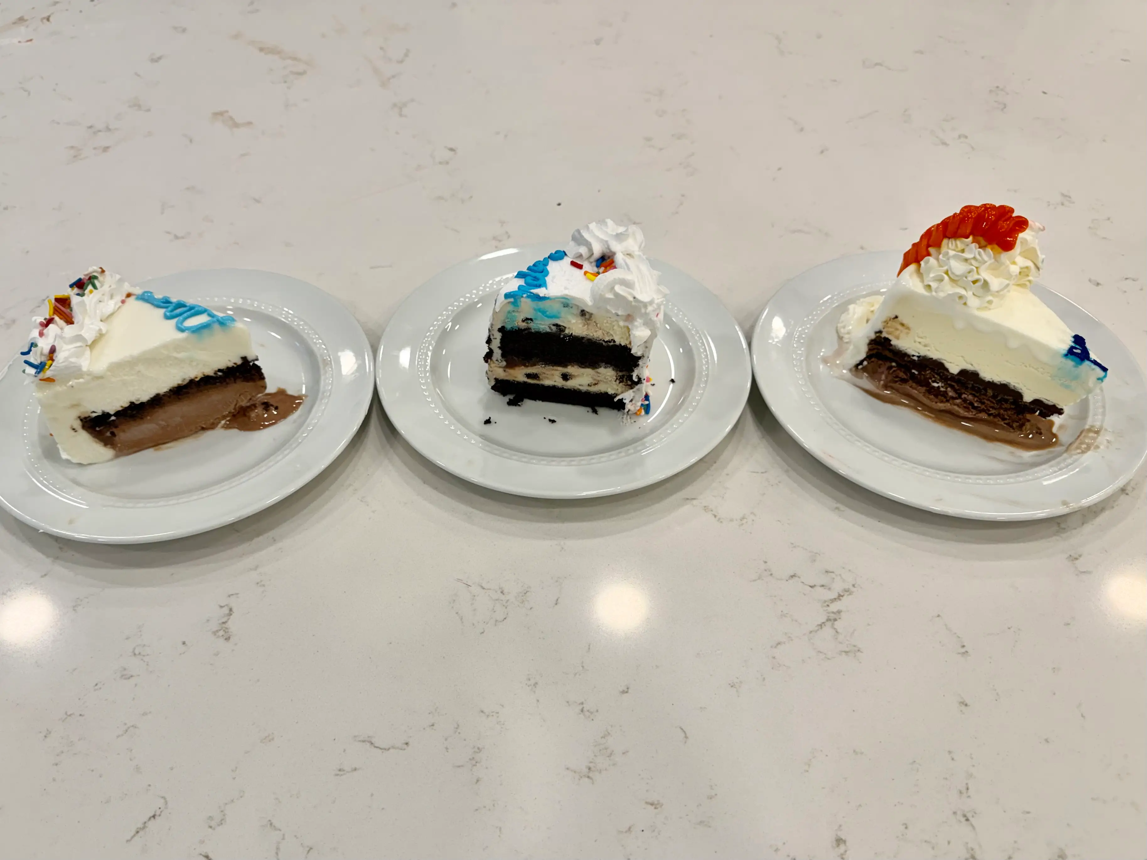 Slices of white ice cream cakes from Dairy Queen, Cold Stone Creamer, and Baskin Robbins on marble counter