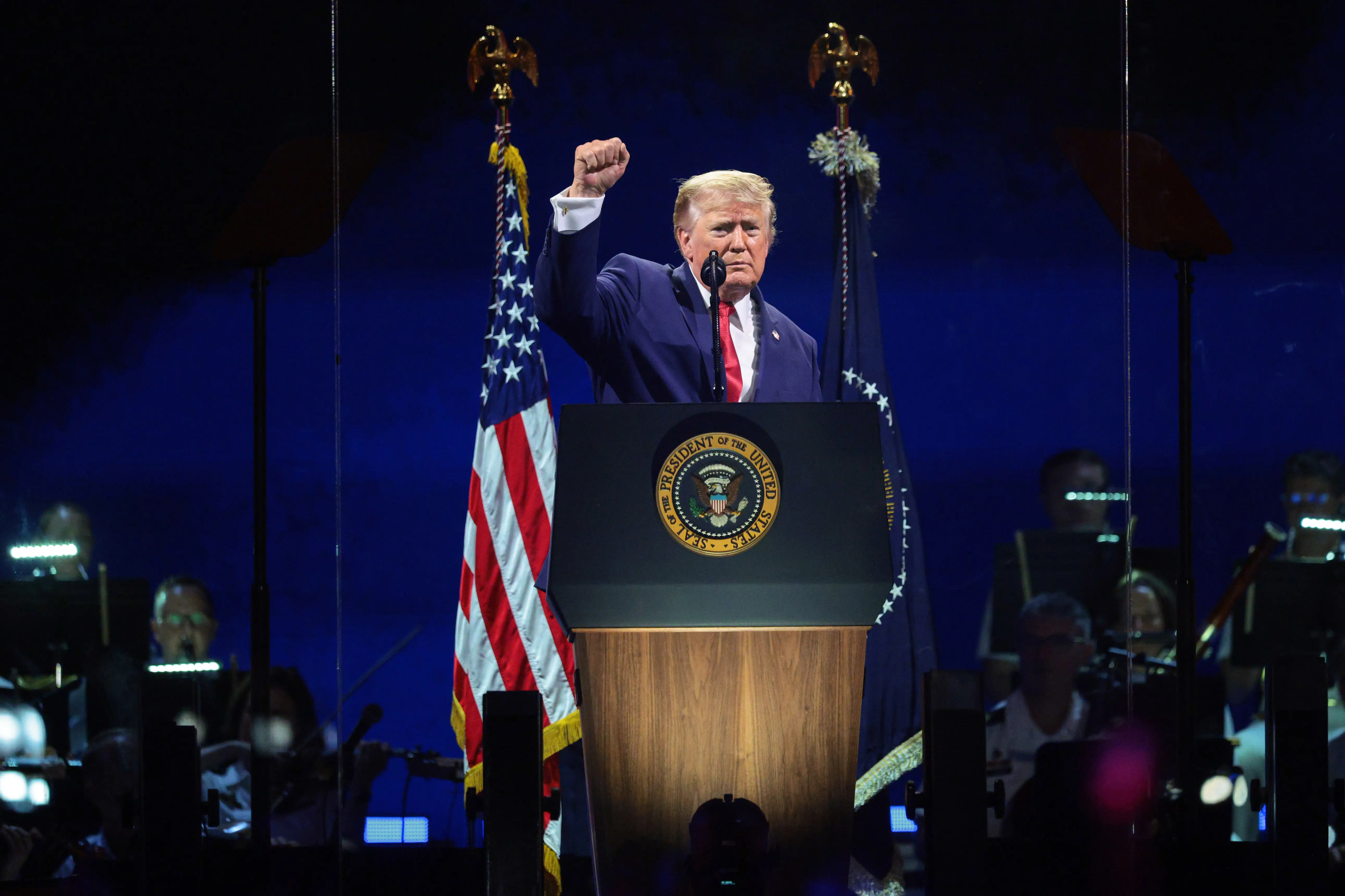 President Donald Trump holds up his right fist as he speaks at a lectern.