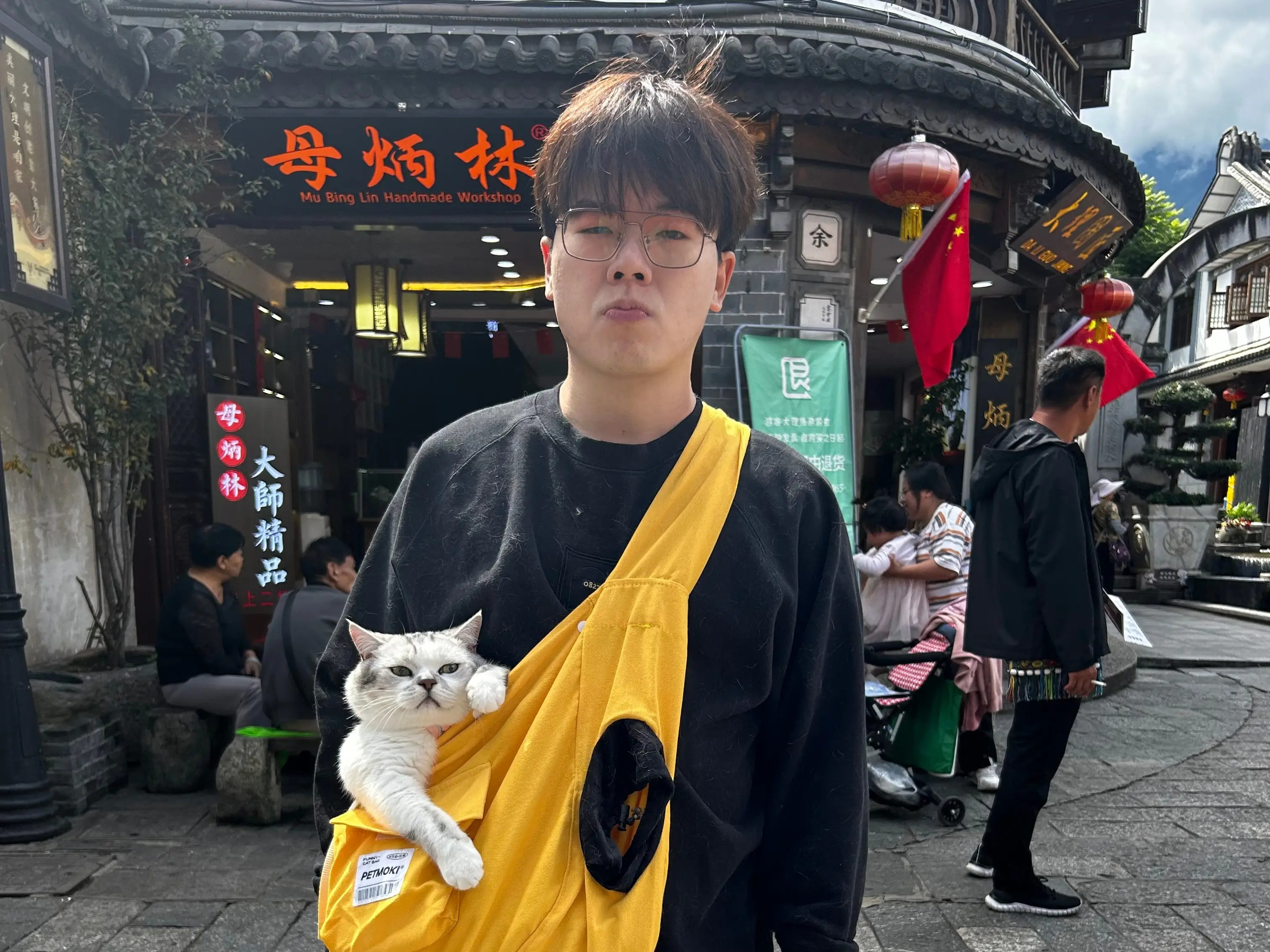 A man standing with a cat in his bag on a street in China.