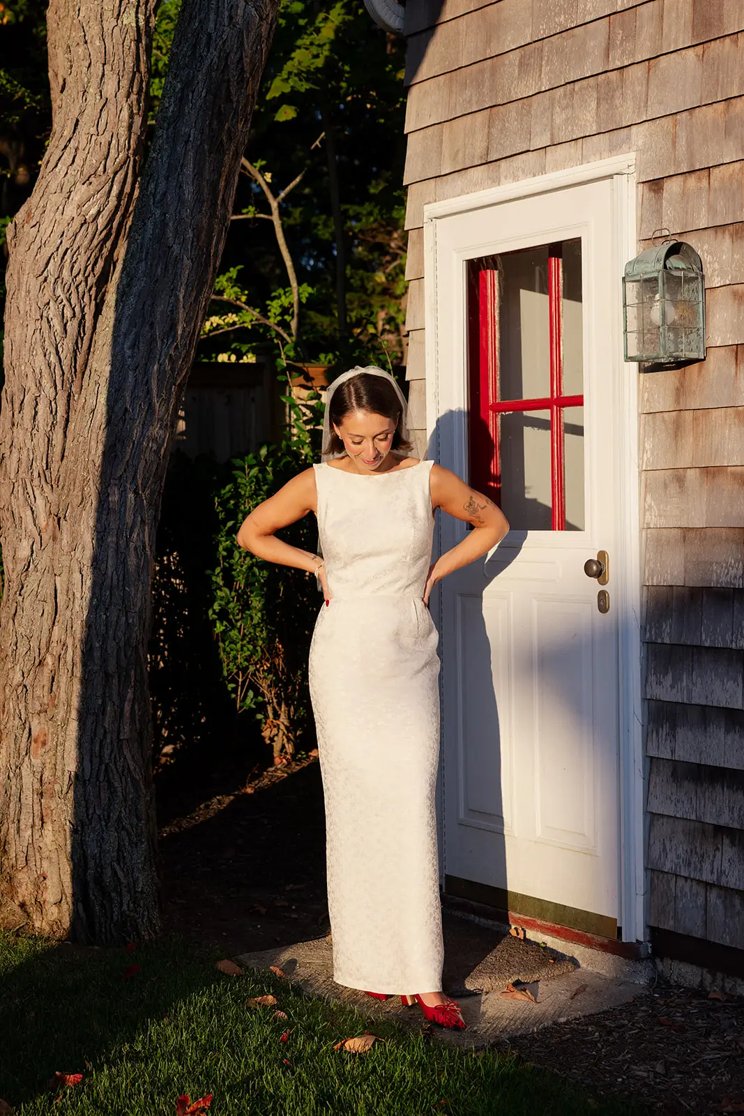 A bride stands in her wedding dress and red shoes in front of a white door with red detailing.