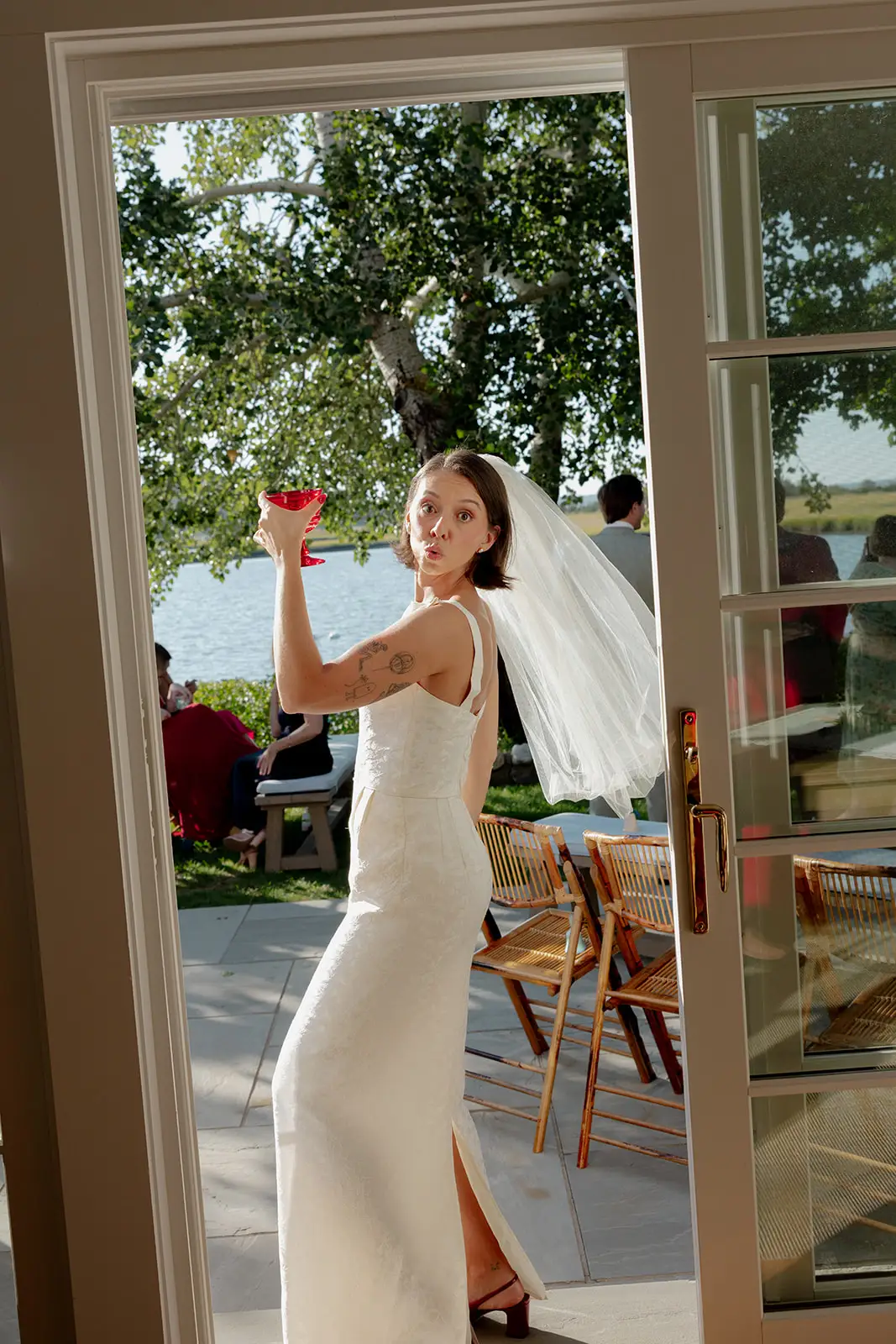 A bride stands in a doorway holding a red cup.