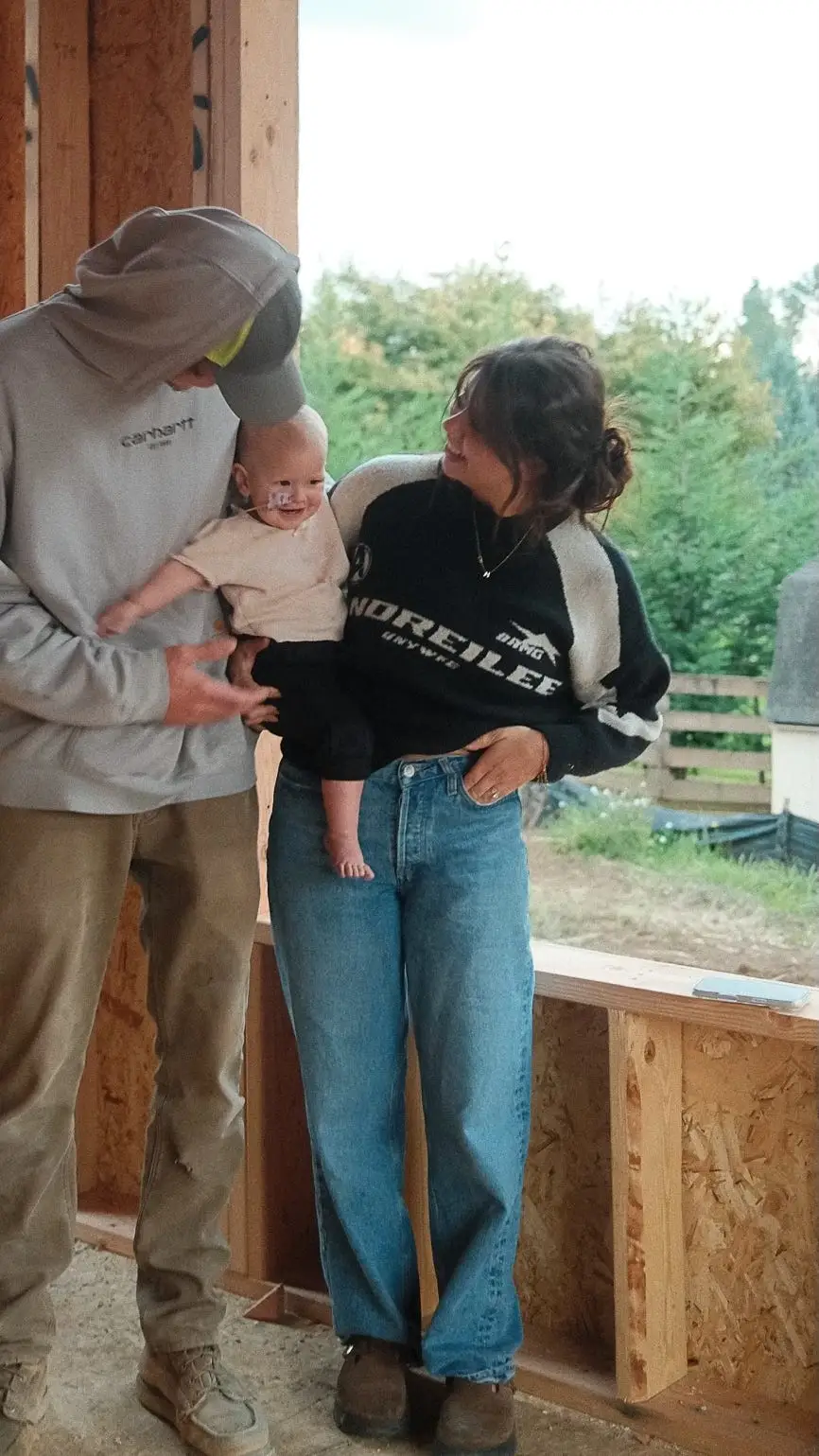 A couple holds their daughter in a house that's under construction.