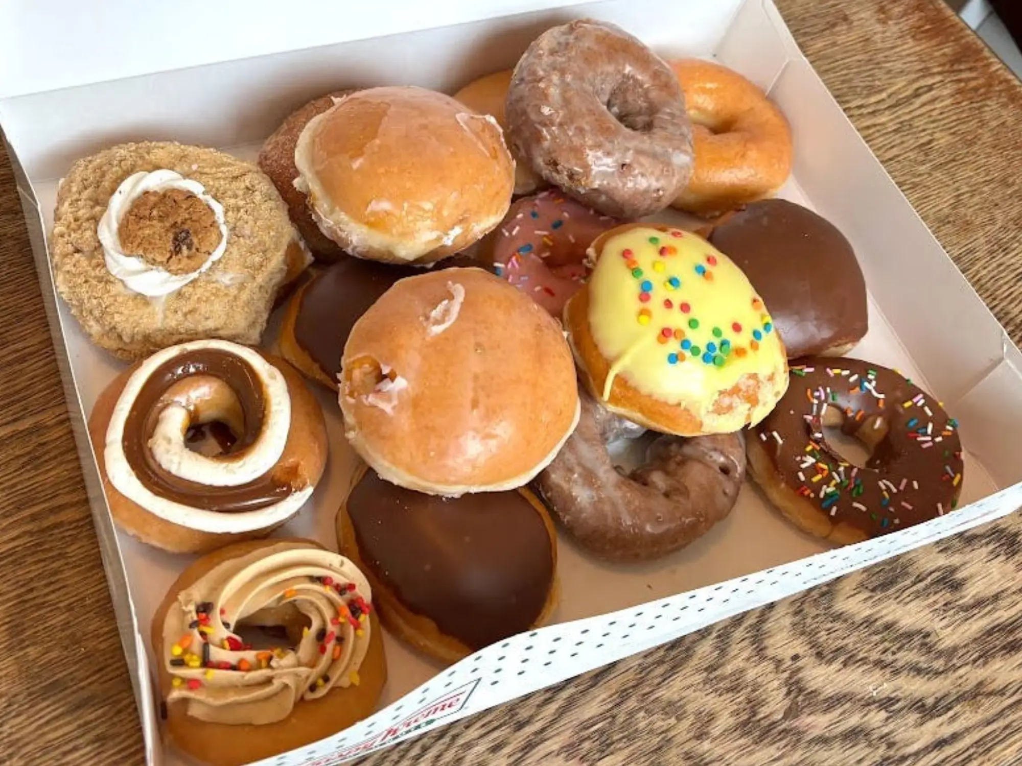 A box of assorted Krispy Kreme doughnuts, with some stacked on top of each other.