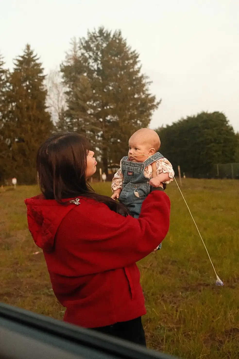 A woman holds her baby up in front of a grassy lot.