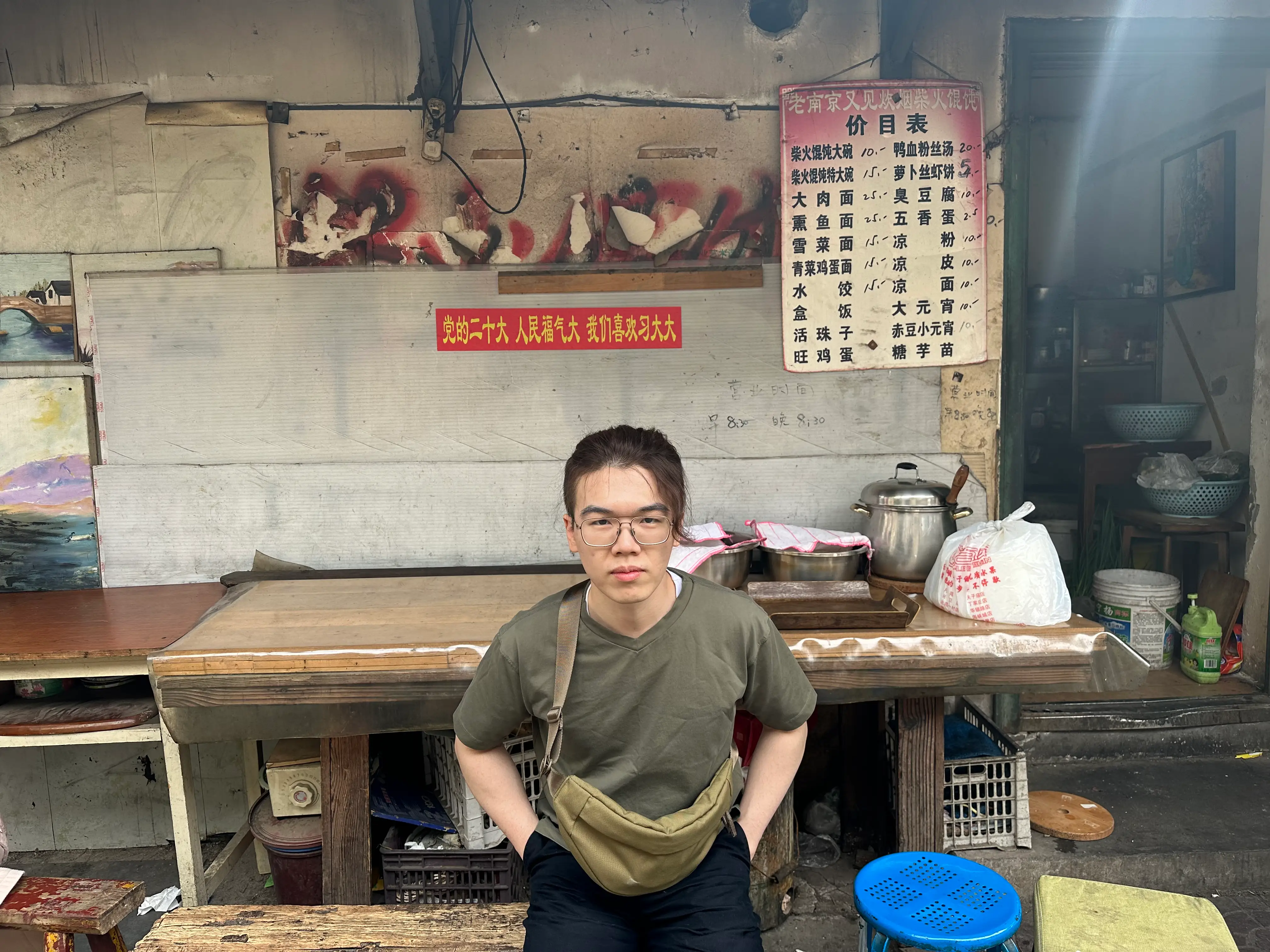 A young man with glasses with signs written in Chinese behind him.