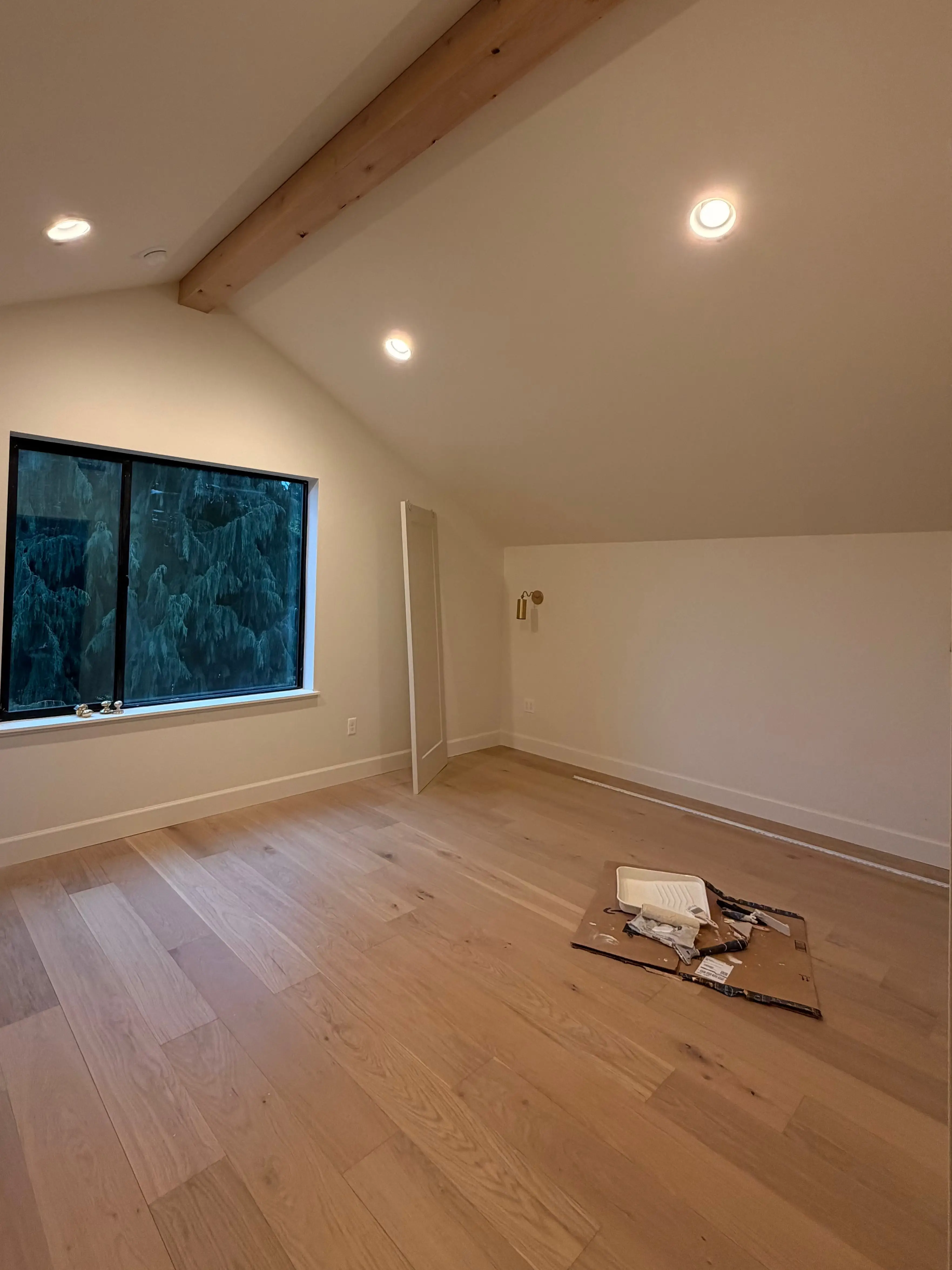 A bedroom with a wooden beam on the vaulted ceiling and a large window on the back well.