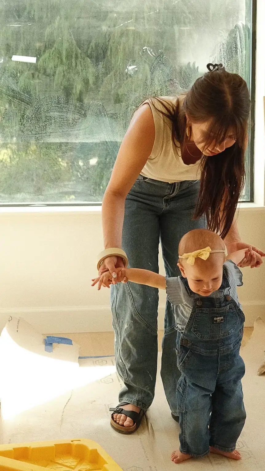 A woman holds her daughters' hands as they walk through their house.