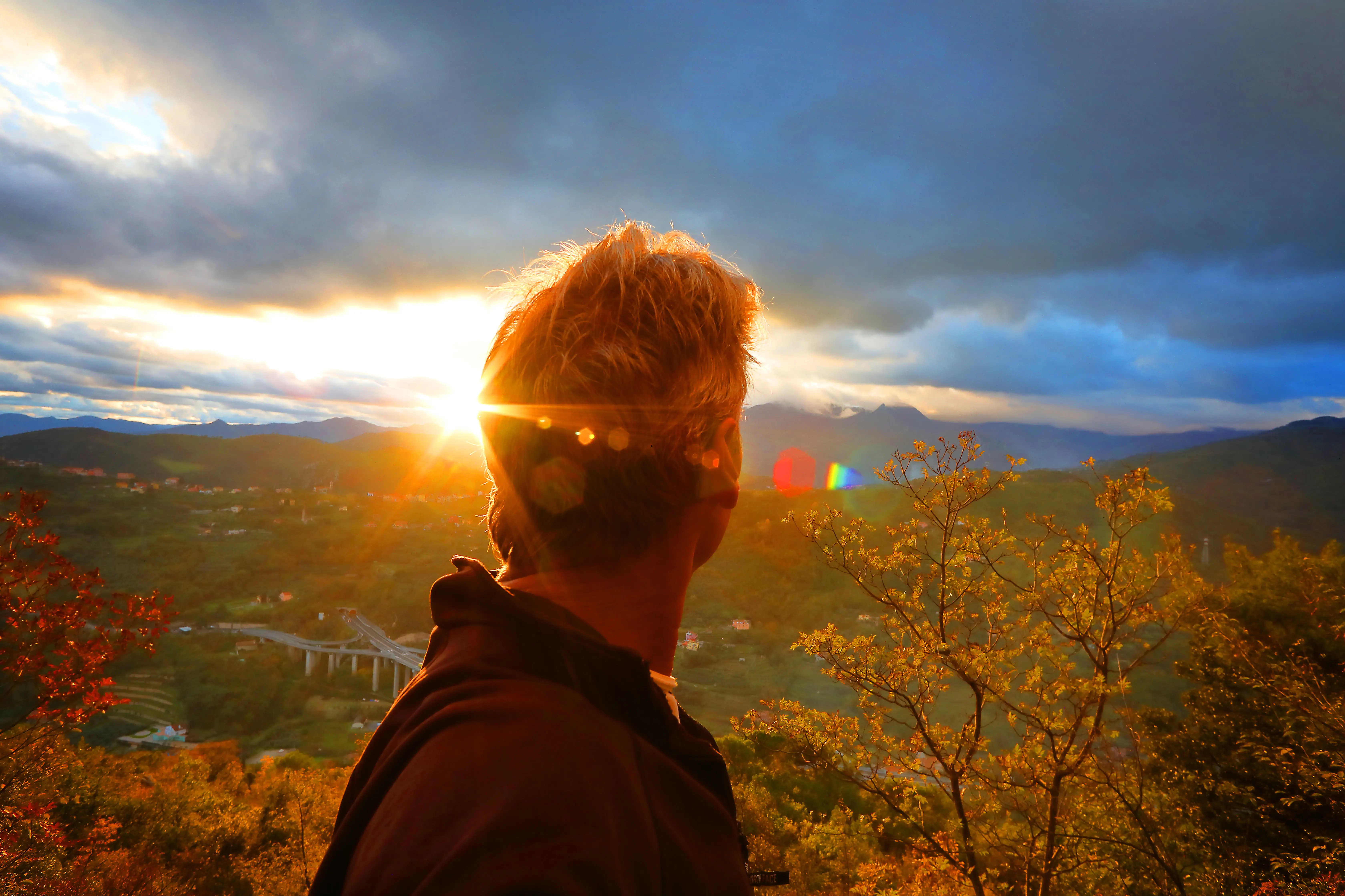 Man looks out over autumn forest and valleys at sunset