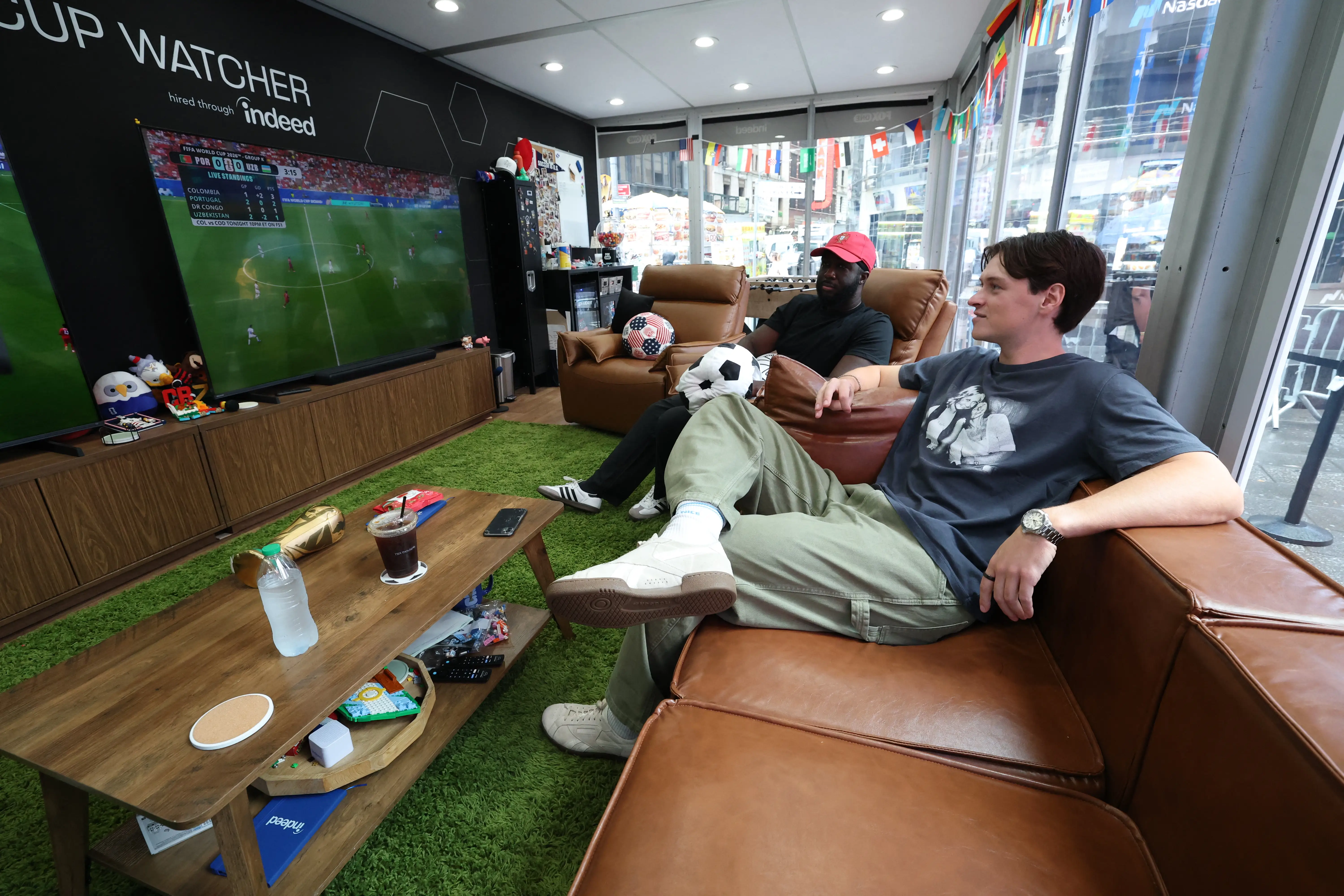 Austin Franklin (right) and Kevin Akoto watch a 2026 World Cup match between Portugal and Uzbekistan from their transparent cube in Times Square in New York, on June 23, 2026. The pair being paid $50,000 by FOX, one of the tournament's broadcasters, were selected from a field of thousands of eager fans after submitting video applications, to watch every one of the 104 games of the World Cup. (