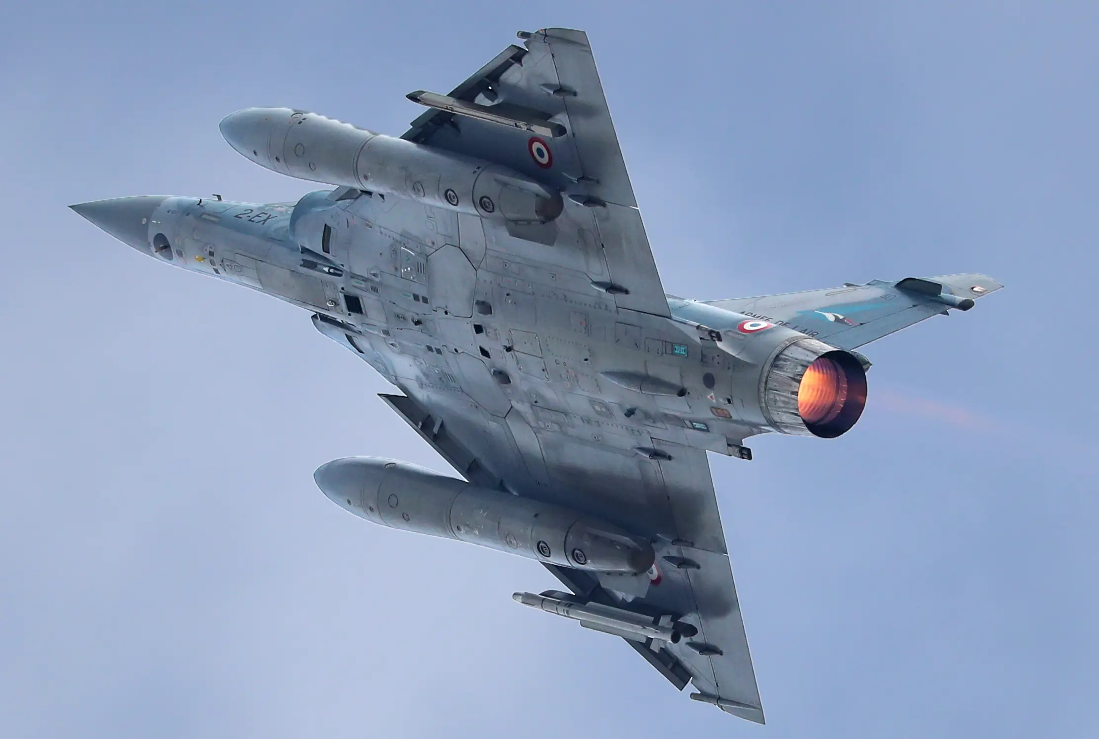 The underside of a grey fighter jet in the air