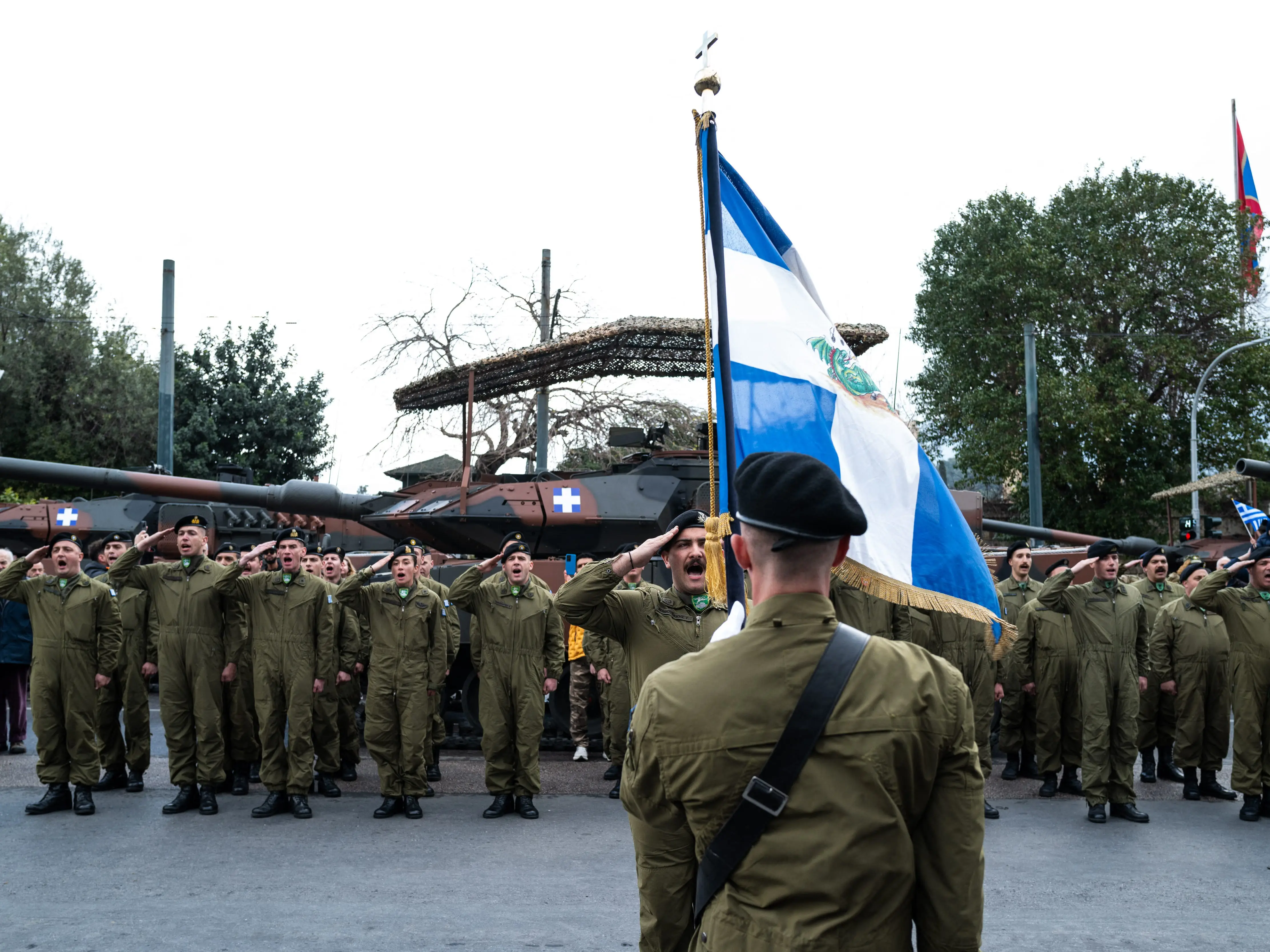 A group of soldiers salute while one holds a Greek flag in front of a line of tanks during a military parade in Athens, Greece on March 25, 2026. The event marks Greece Independence Day, commemorating the 1821 War of Independence with a large annual military parade in the city center.