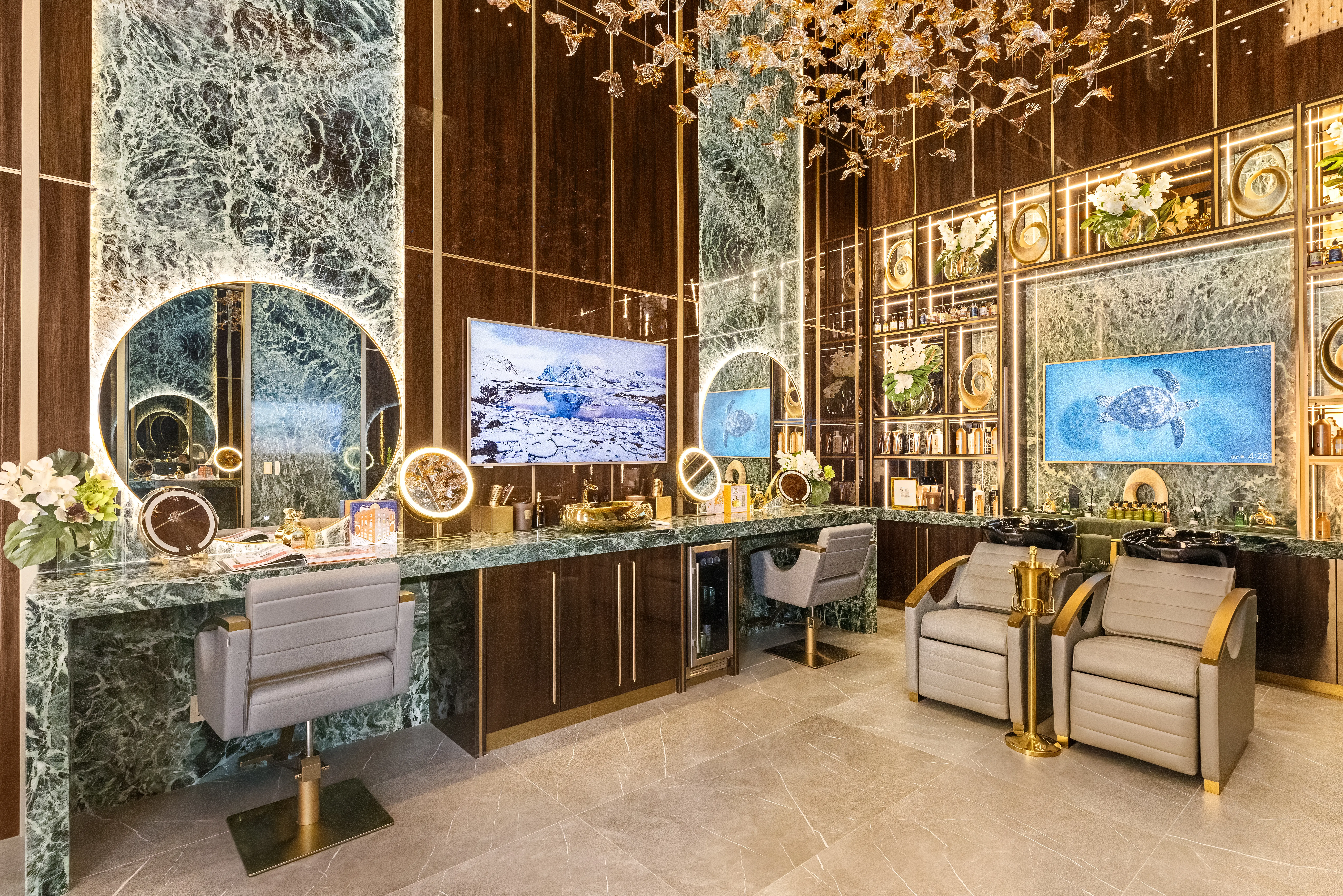 Luxurious salon interior with green marble counters, illuminated mirrors, styling chairs, shampoo chairs, shelves, and floral decor.