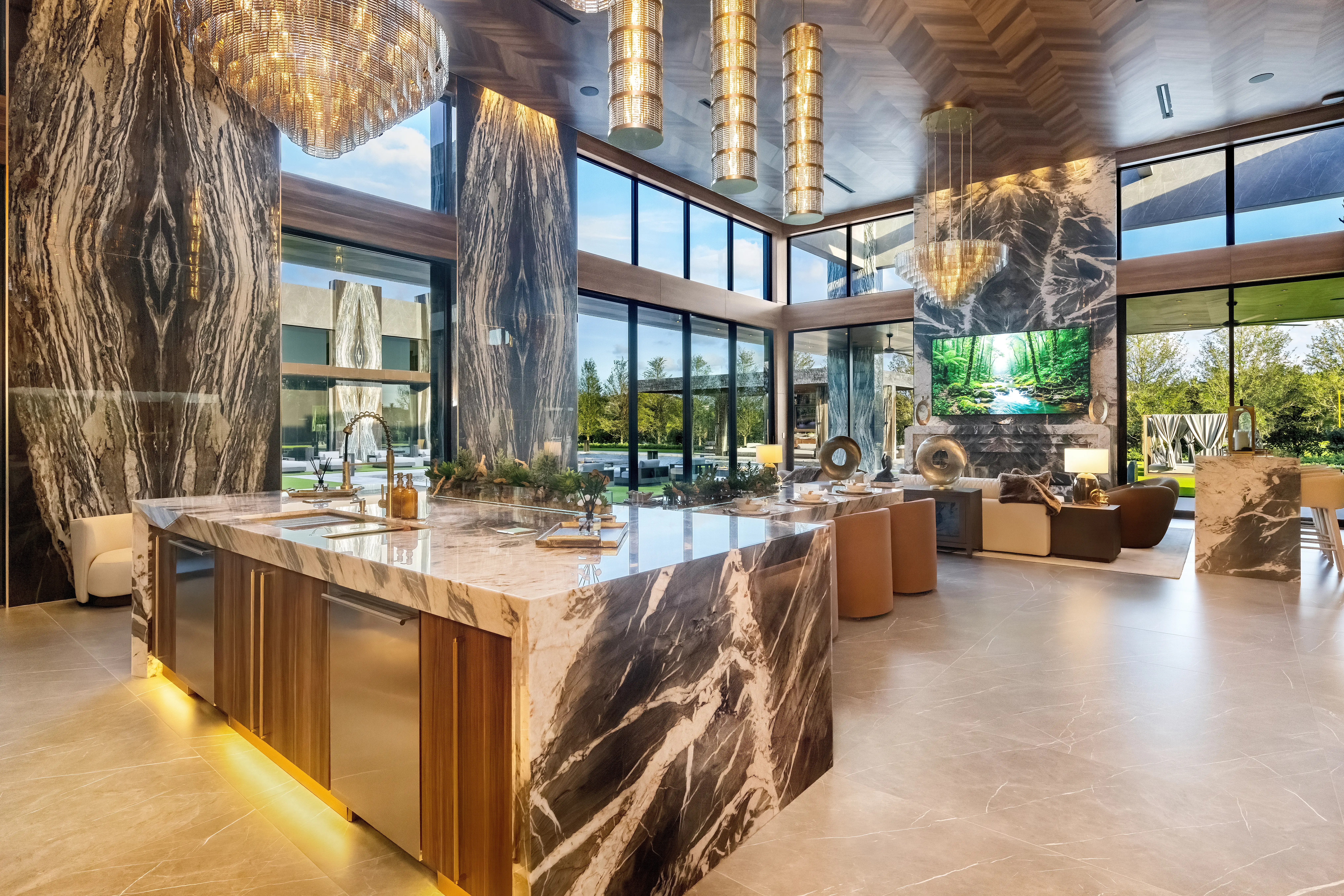 Luxury open-plan kitchen and living area with marble finishes, chandeliers, large windows, and modern seating.