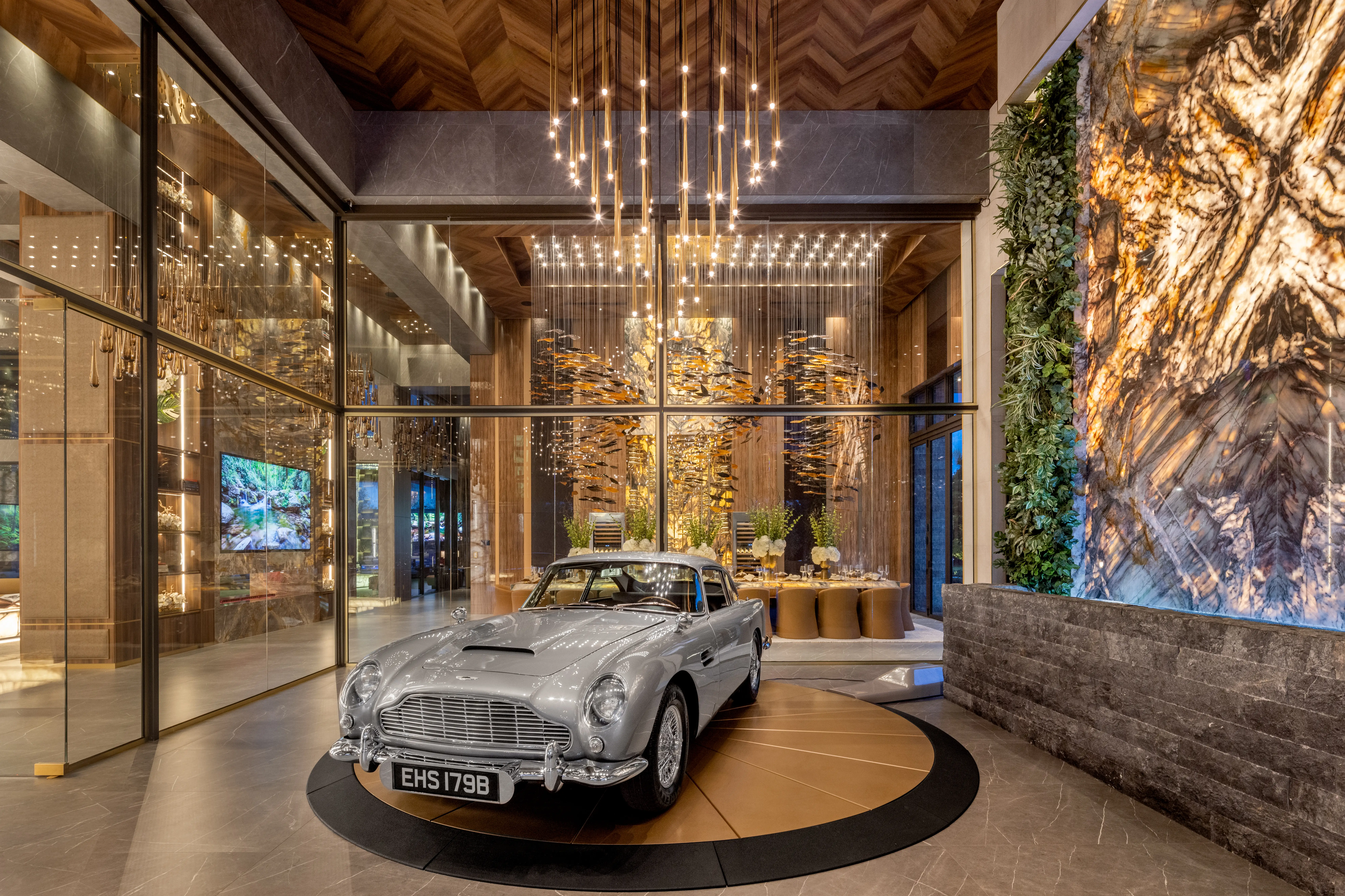 Classic silver Aston Martin car displayed on a circular platform in a modern luxury interior lobby.