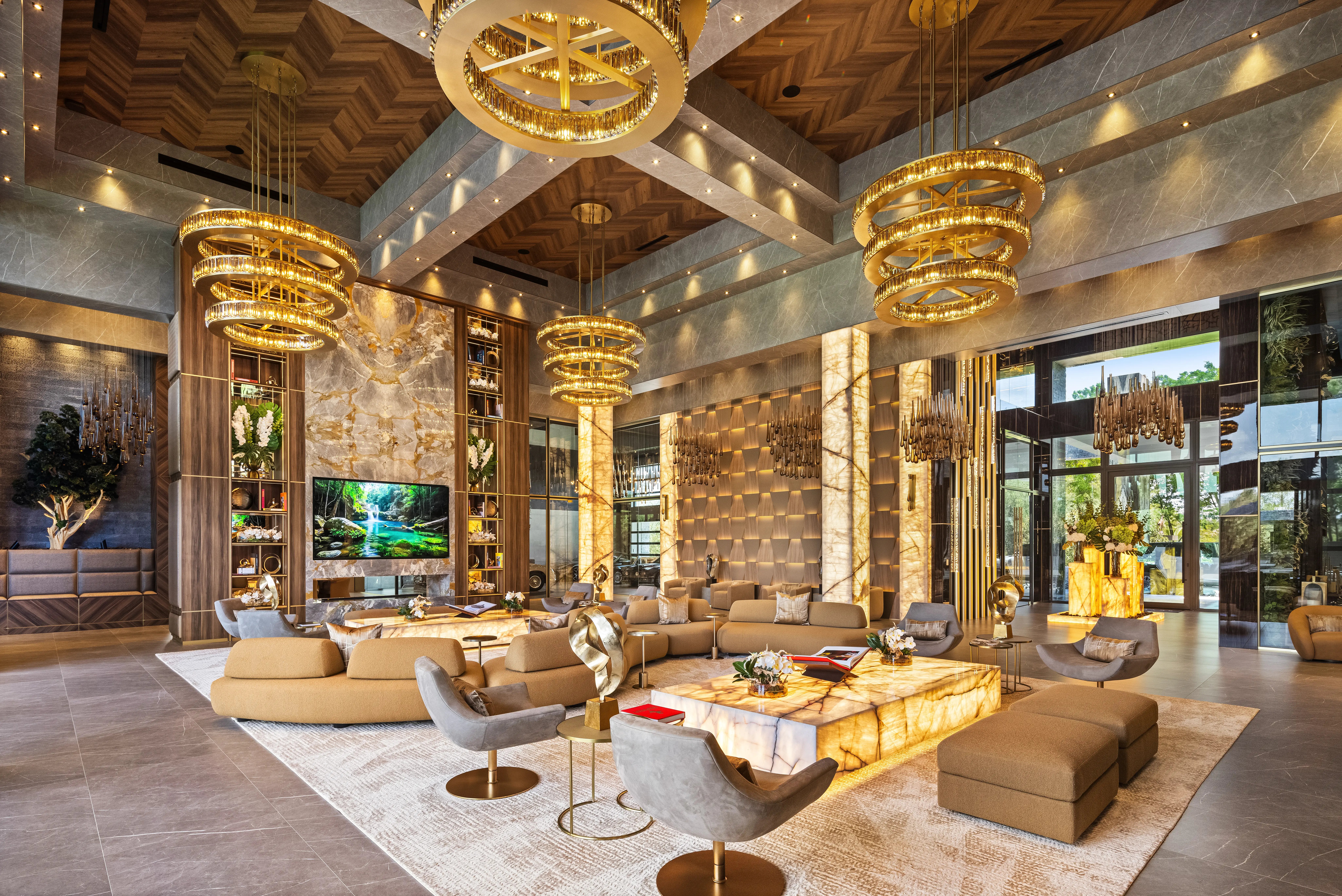 Luxury lounge interior with gold chandeliers, marble finishes, sofas, armchairs, and large windows.