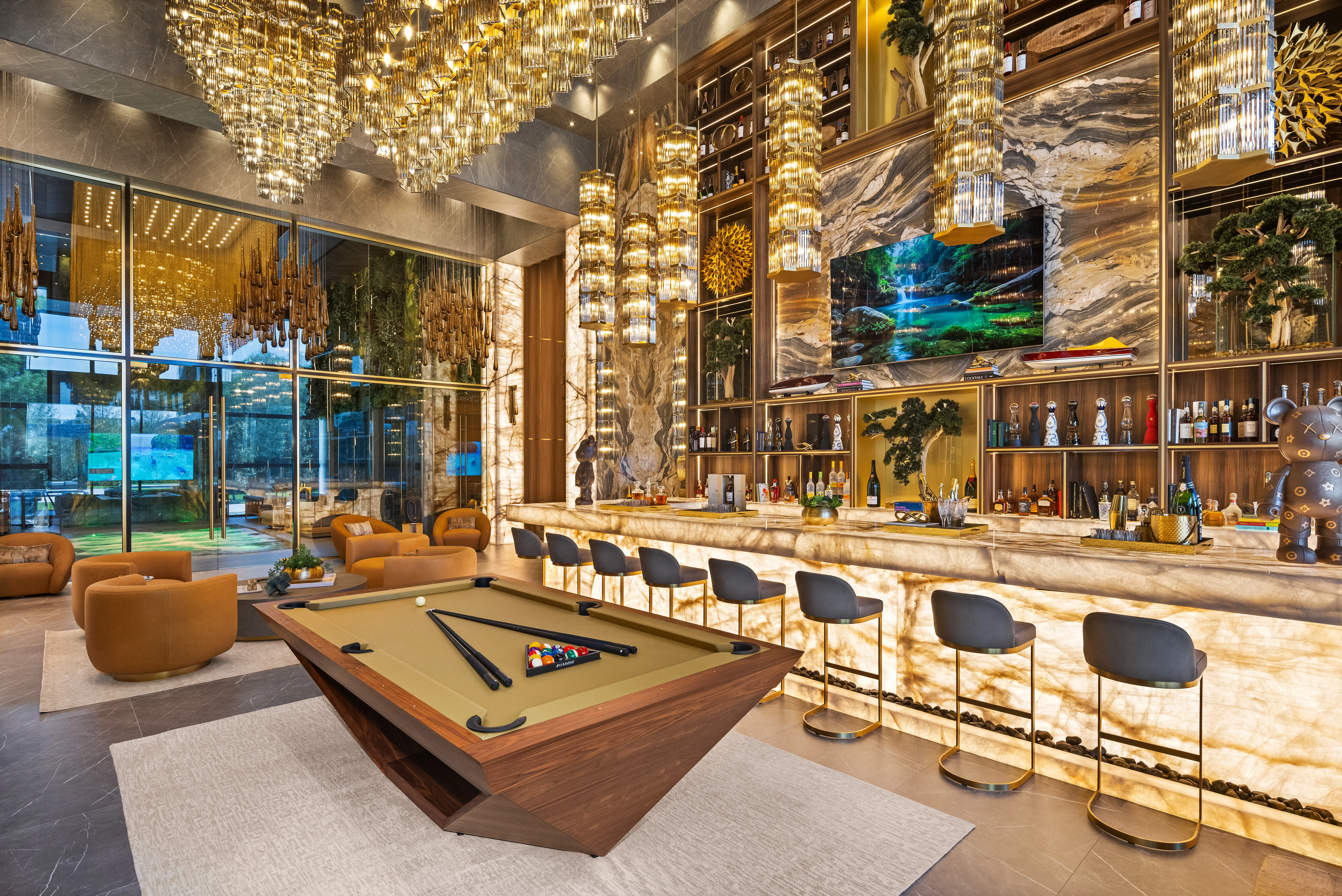 Luxurious lounge bar with illuminated chandeliers, marble shelving, bar stools, seating area, and a central pool table.
