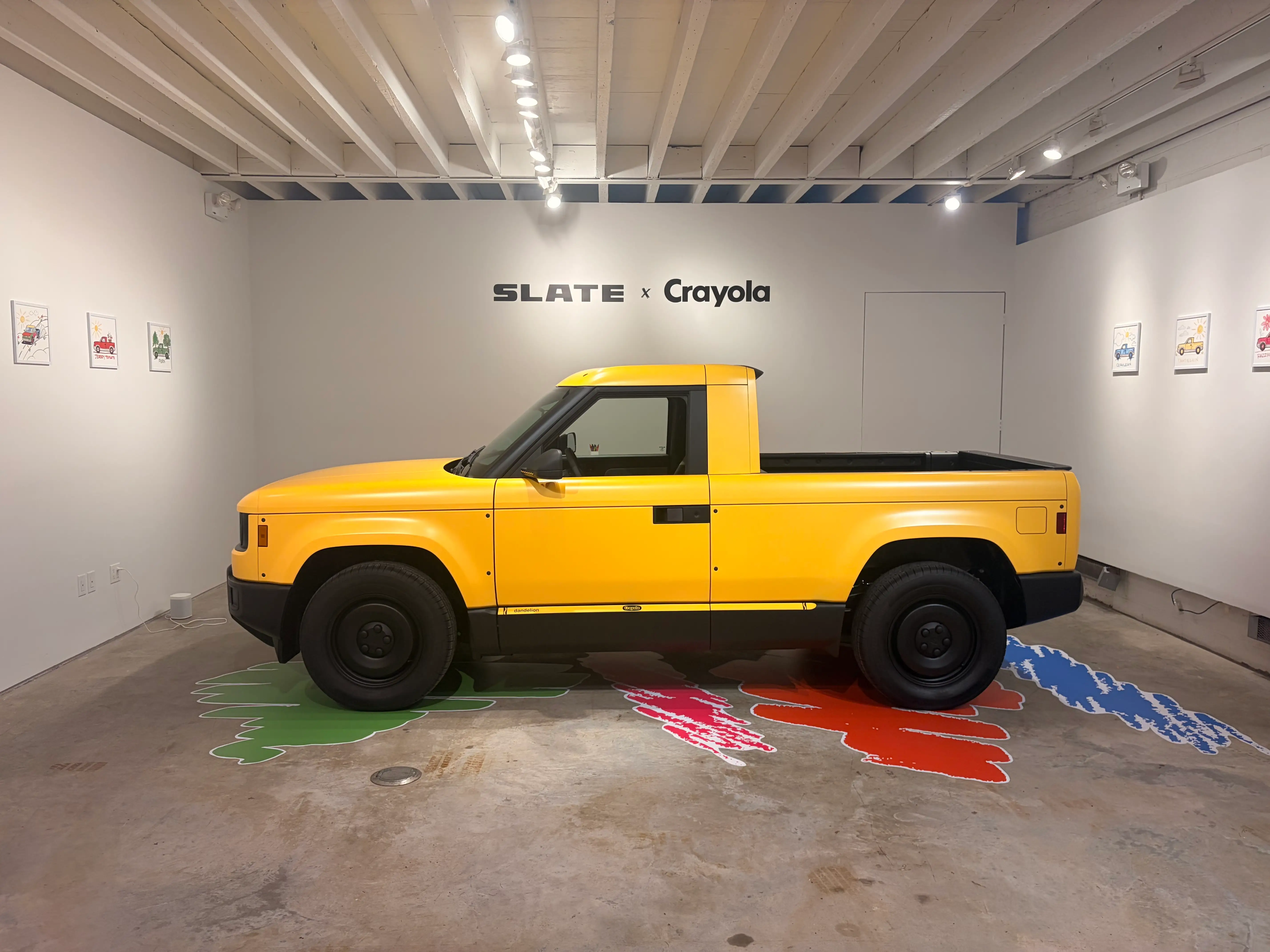 A bright yellow Slate Truck is parked on a showroom floor with decals of other Crayola colors.
