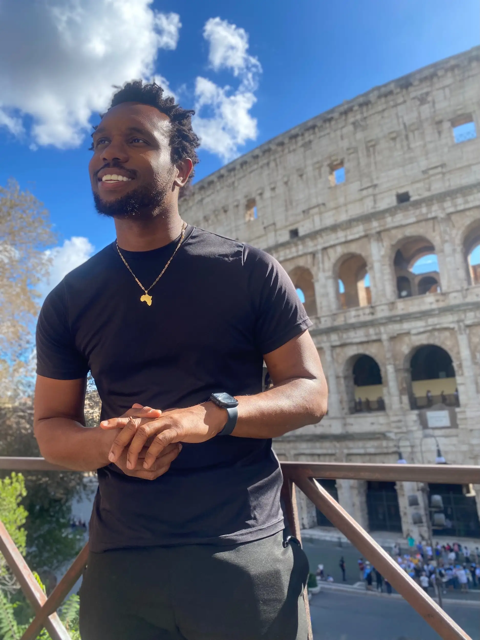 Person standing on a balcony near the Colosseum under a bright blue sky.