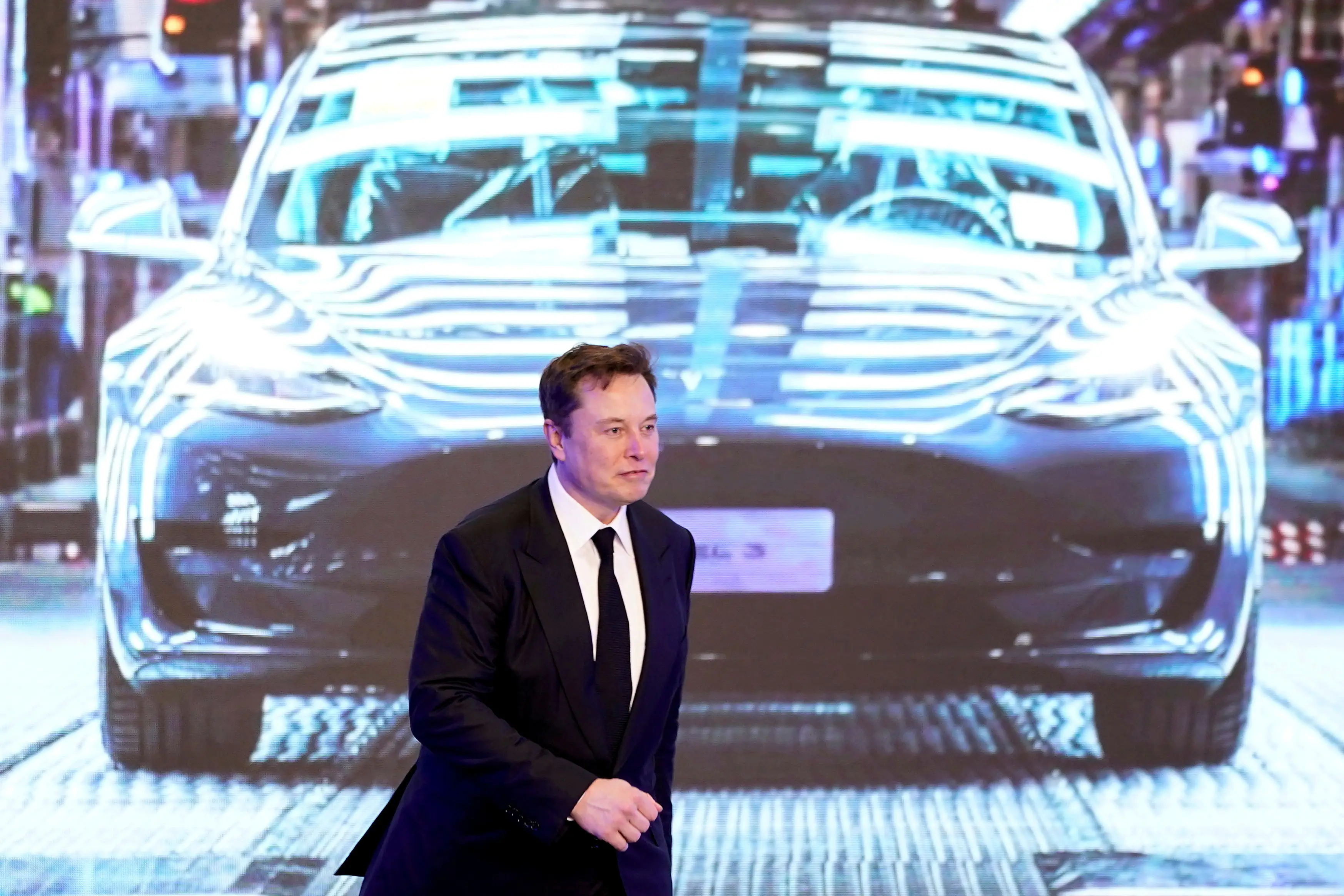 Tesla CEO Elon Musk walks next to a screen showing an image of Tesla Model 3 during an opening ceremony for Tesla's Model Y program in Shanghai, China.