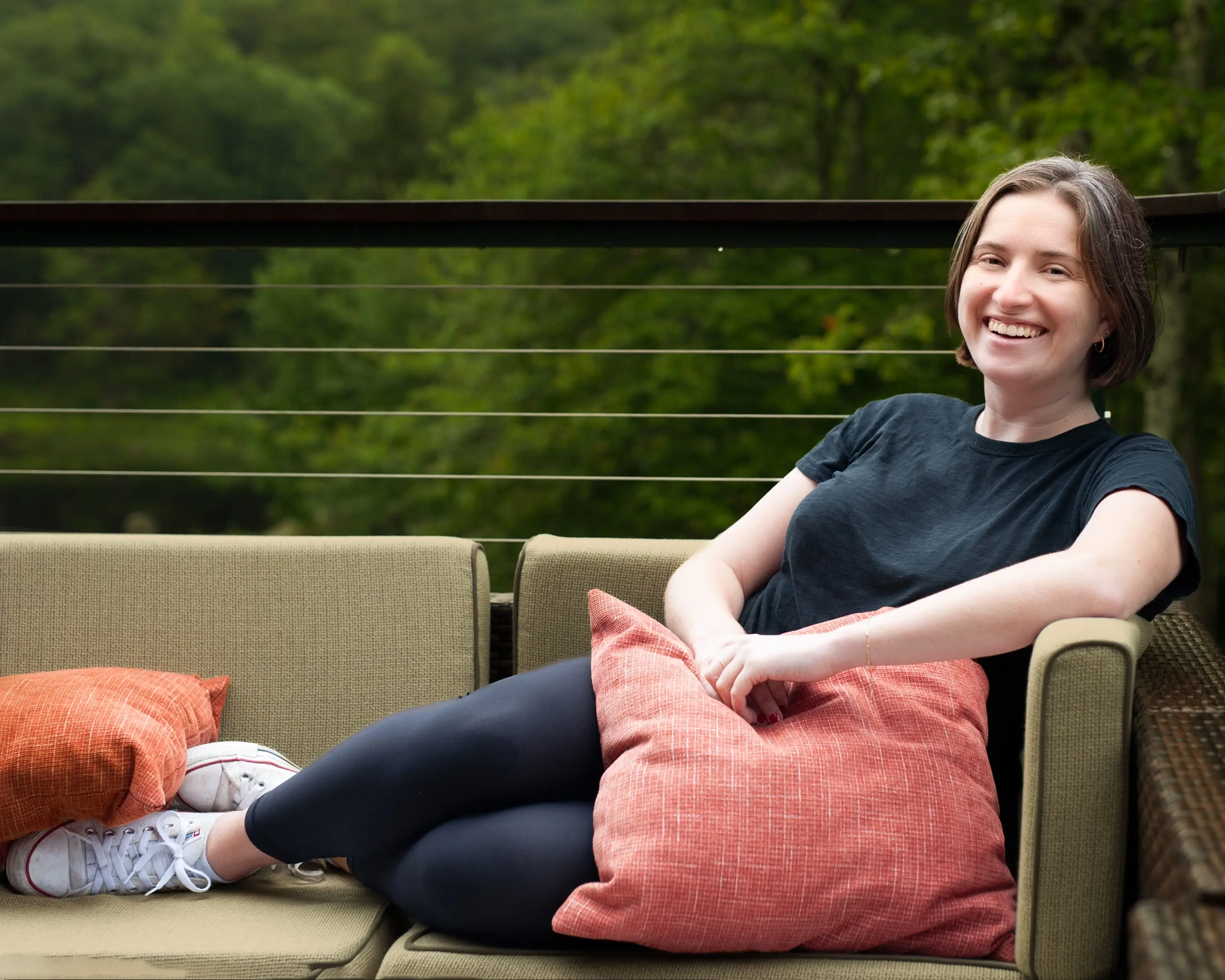 A young woman smiles while lying on a couch on a deck.